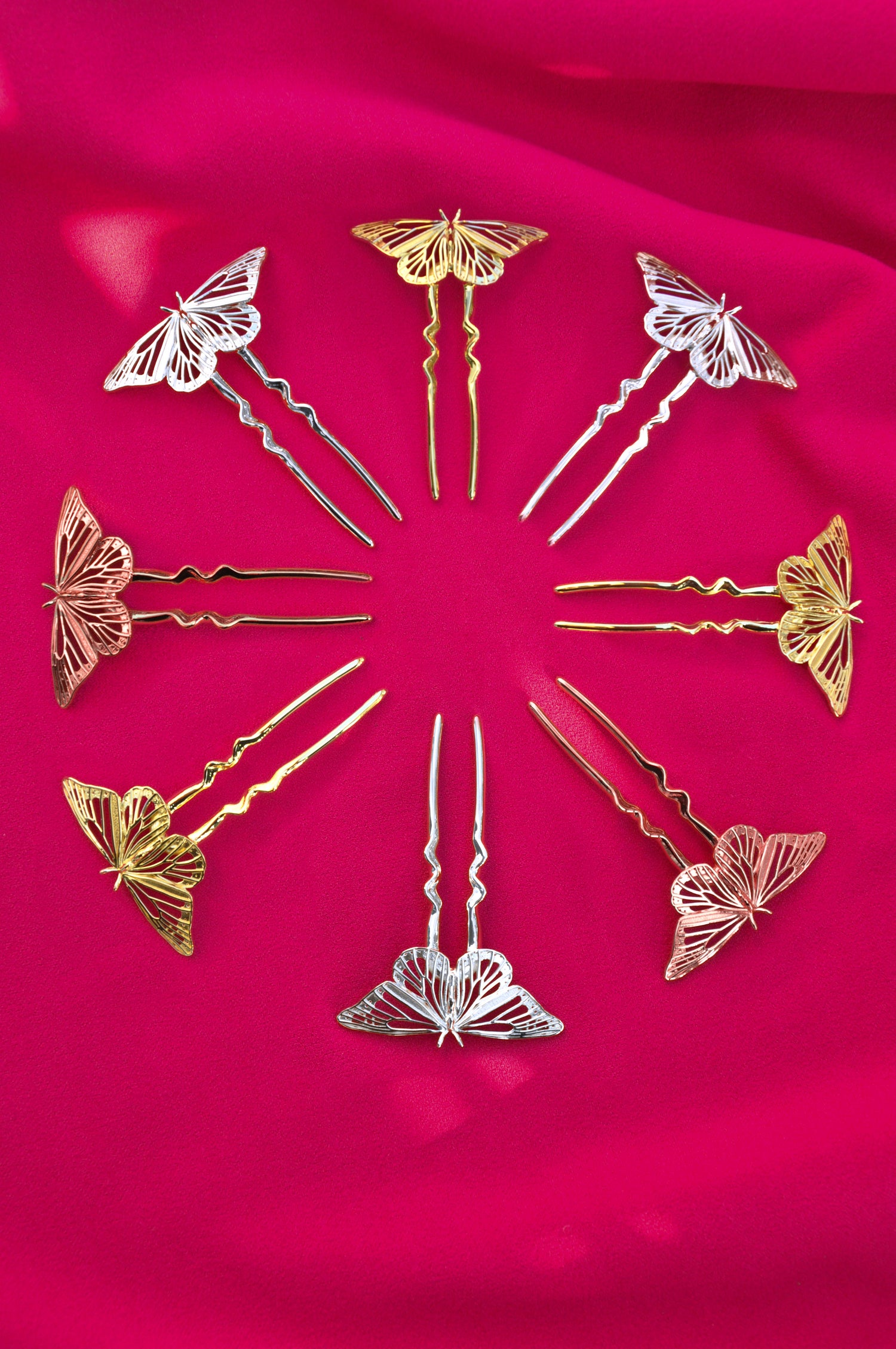 Gold and silver hairpins with butterfly designs arranged in a circular pattern on a pink fabric background.