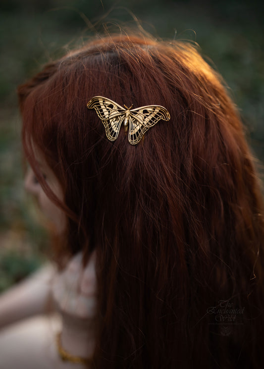 Close-up of model wearing Atlas Moth hair comb in a natural outdoor setting, showcasing handcrafted insect-inspired jewelry with detailed wing design and metallic finish.