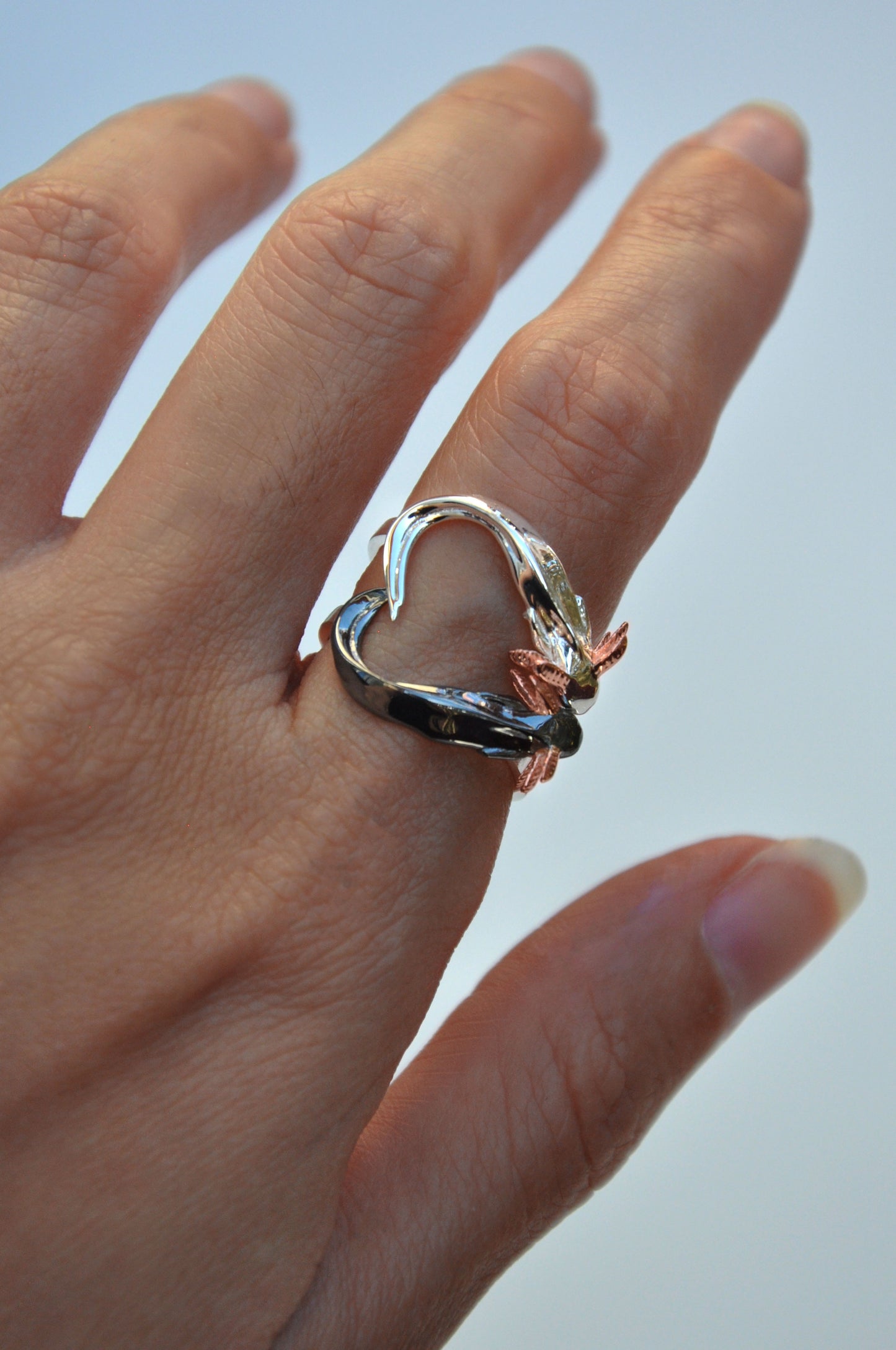 Front view of handcrafted Axolotl Stacking Ring Set forming a heart shape with tails — sterling silver and black rhodium axolotls with 14k rose gold gills.