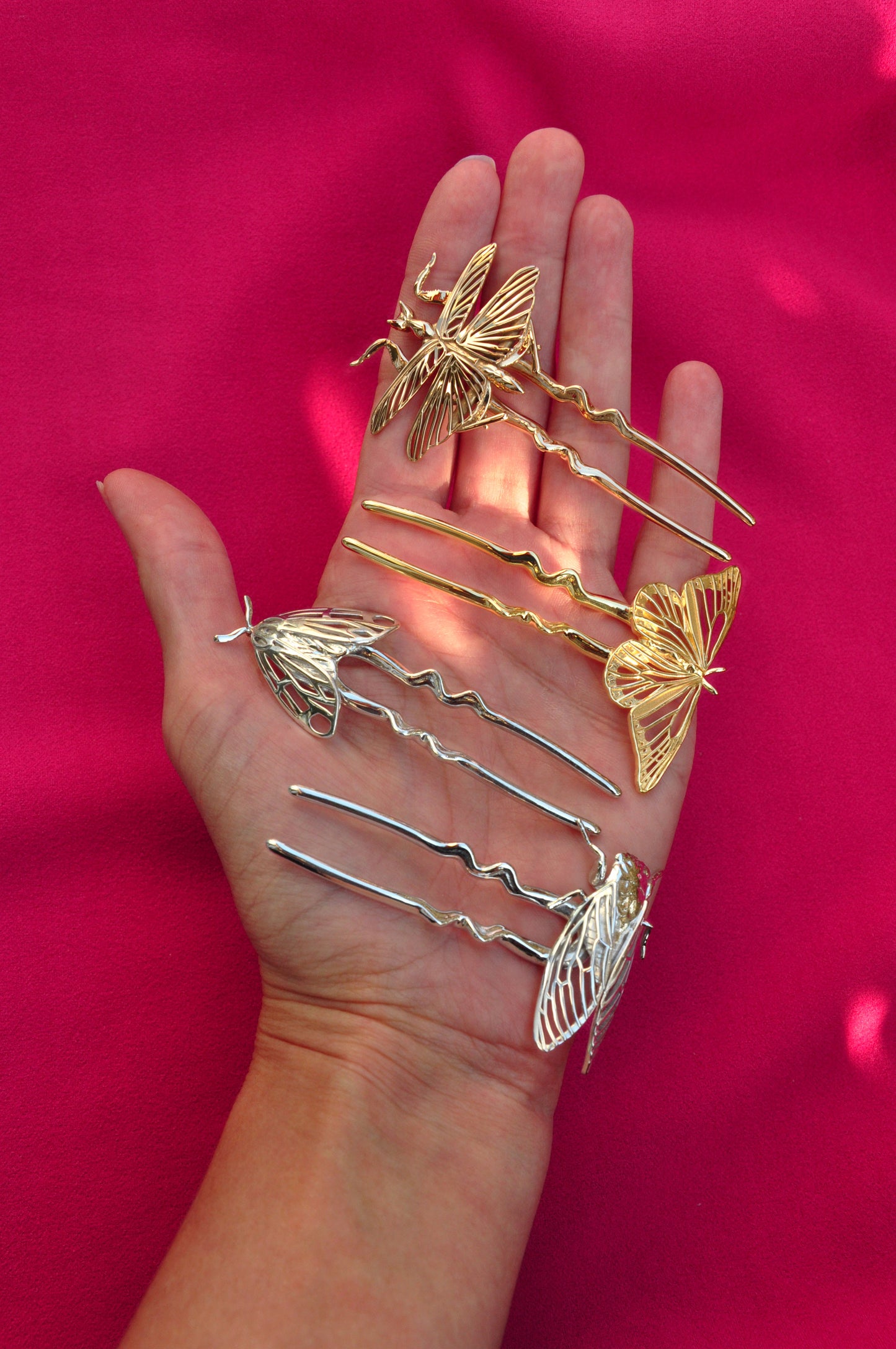 Hand holding gold hair pins against a pink background