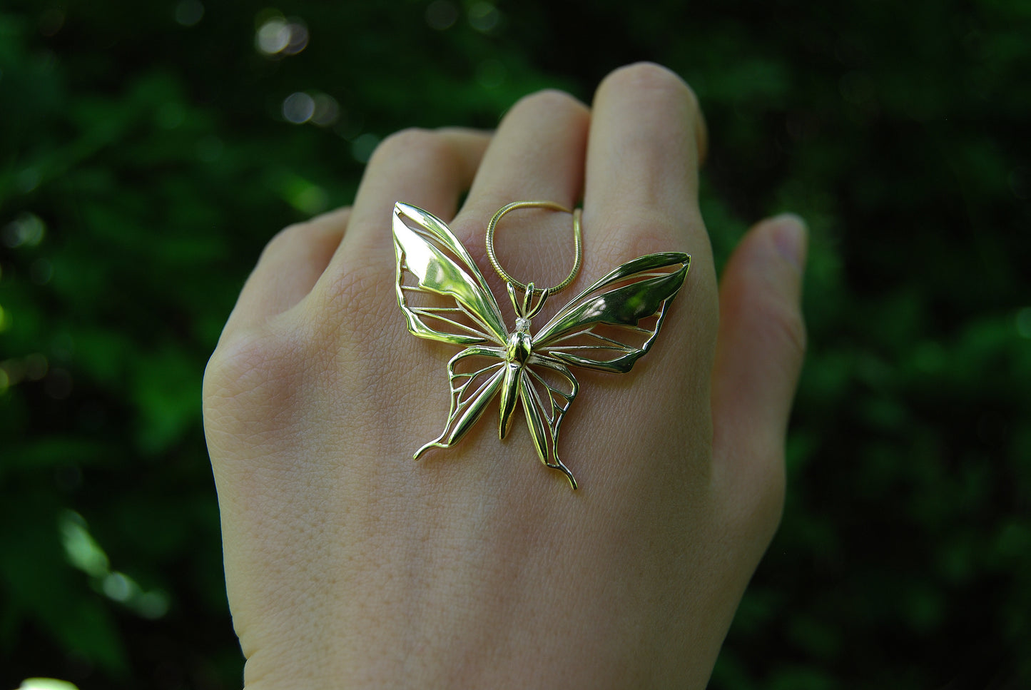 Close-up of gold butterfly pendant necklace held in hand