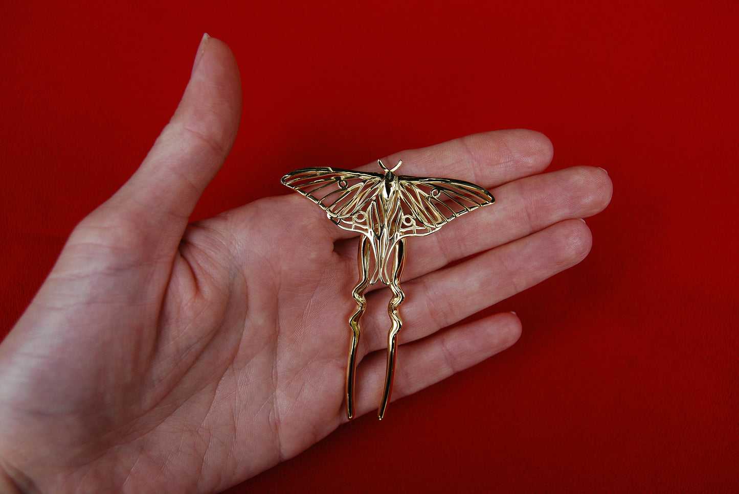 Close-up of a hand holding a 14k gold-plated Luna Moth hair pin, highlighting the delicate wing details and polished finish of this nature-inspired insect accessory.