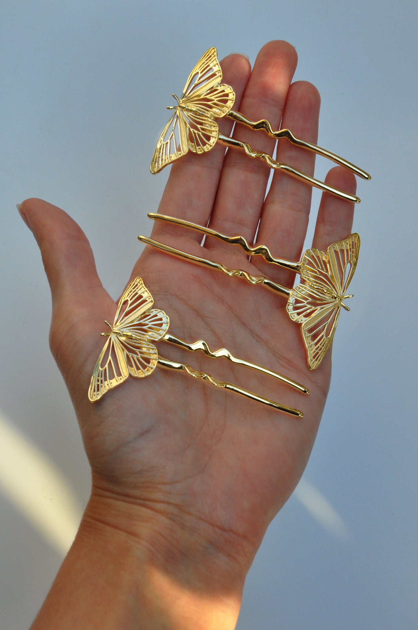 Gold butterfly hairpins held in a hand against a neutral background