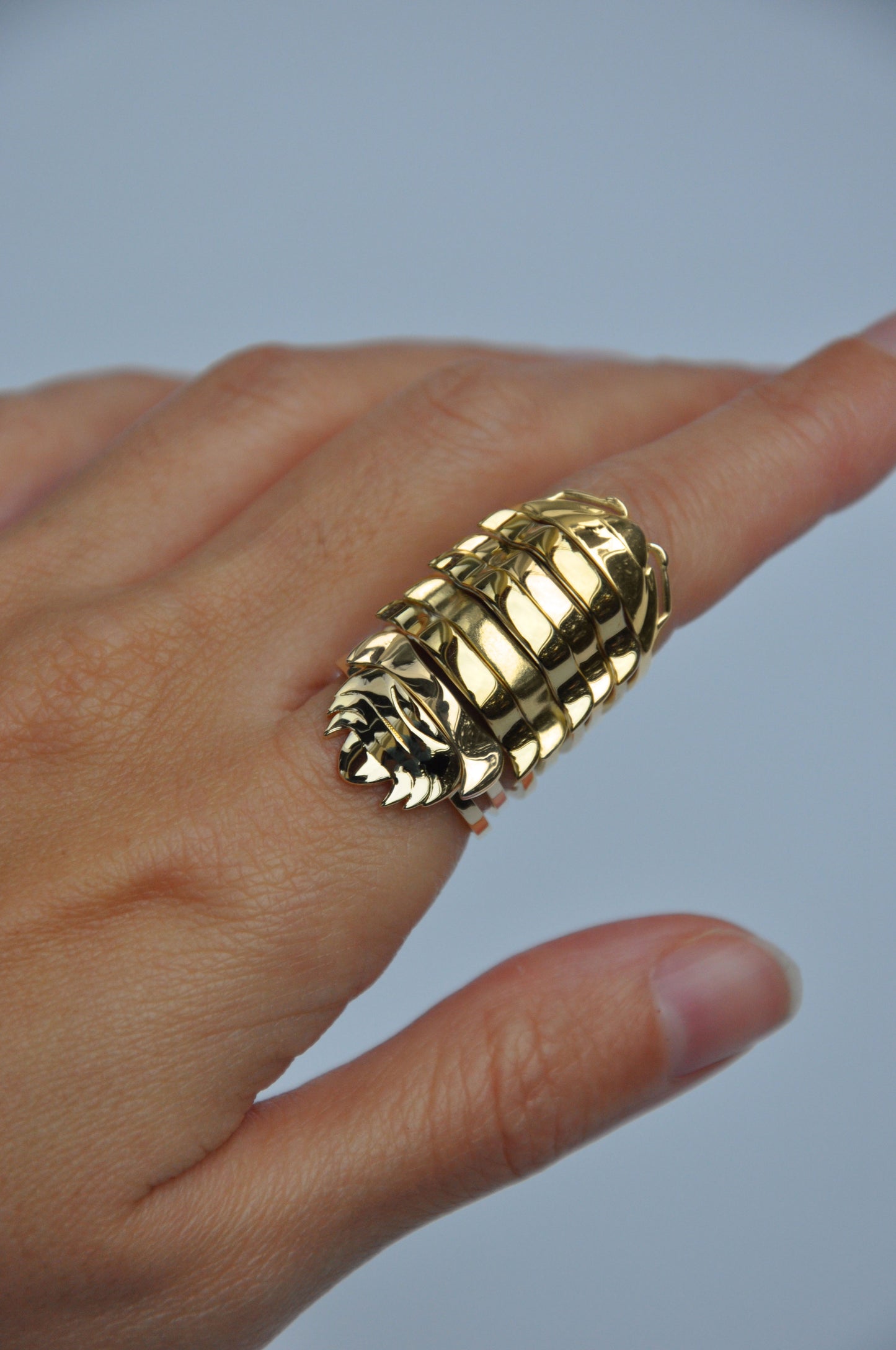 Finger wearing stacked 14k gold-plated isopod rings, inspired by segmented armor and insect design