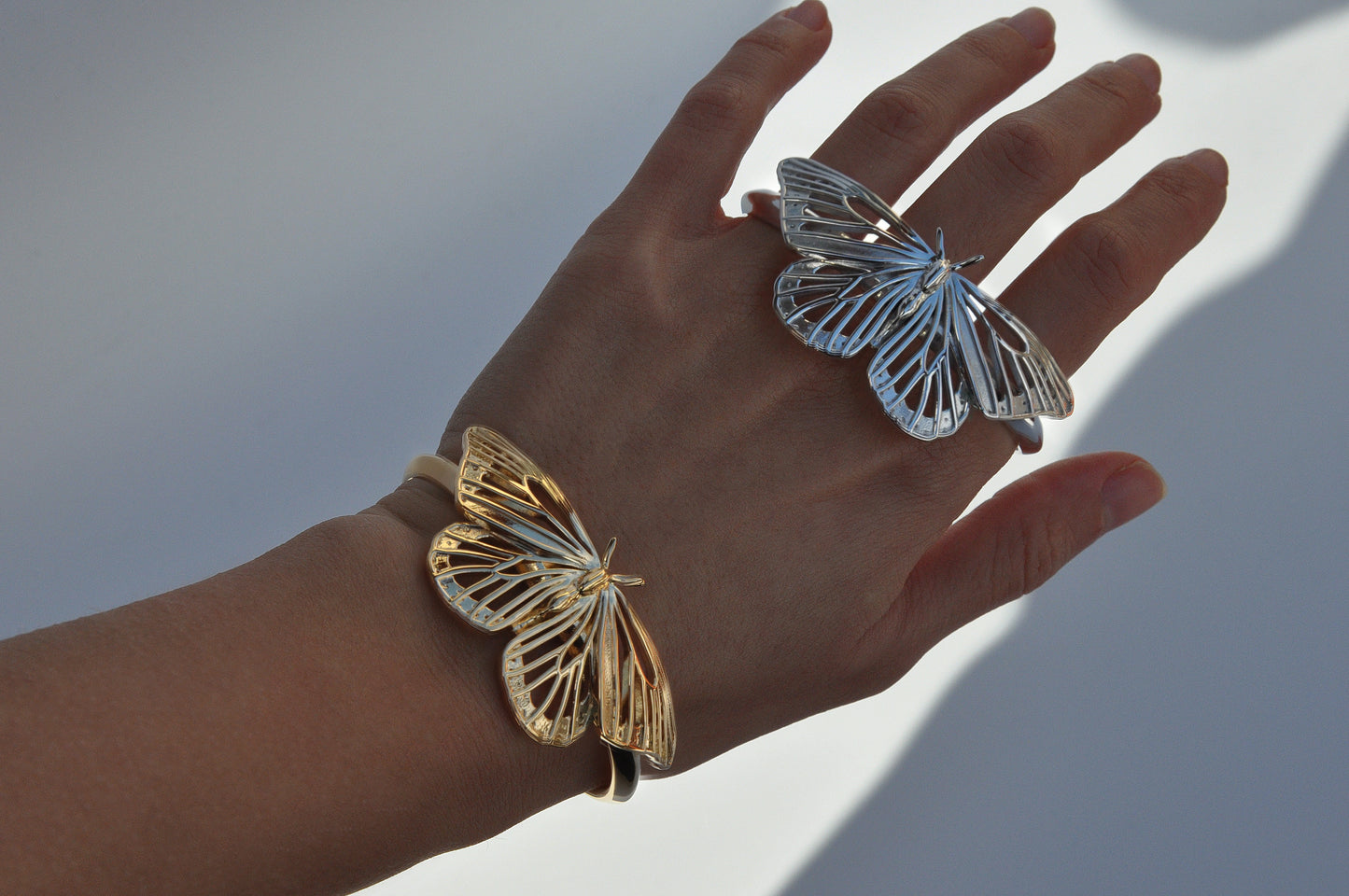 Hand wearing both gold and silver Monarch Butterfly Bracelets, highlighting contrast in finishes and unified design.