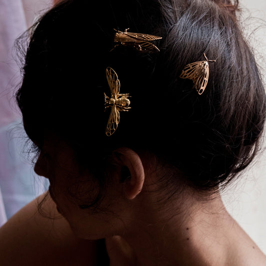 Model wearing bee, tiger moth, and cicada hair pins together in an elegant updo, showcasing gold, silver, and bronze finishes.