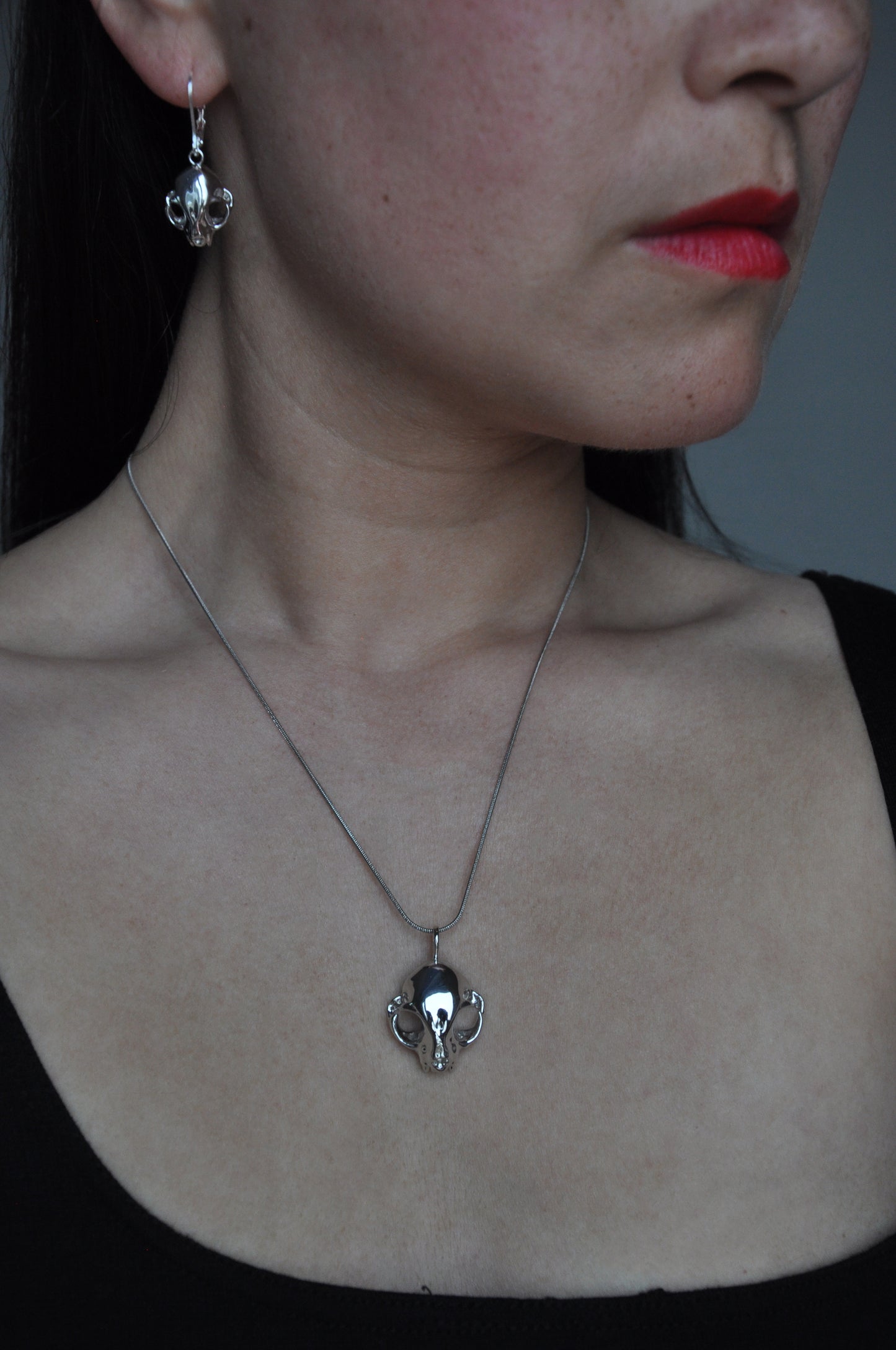 Model wearing the silver feline skull pendant and matching earrings, highlighting the coordinated gothic jewelry set.