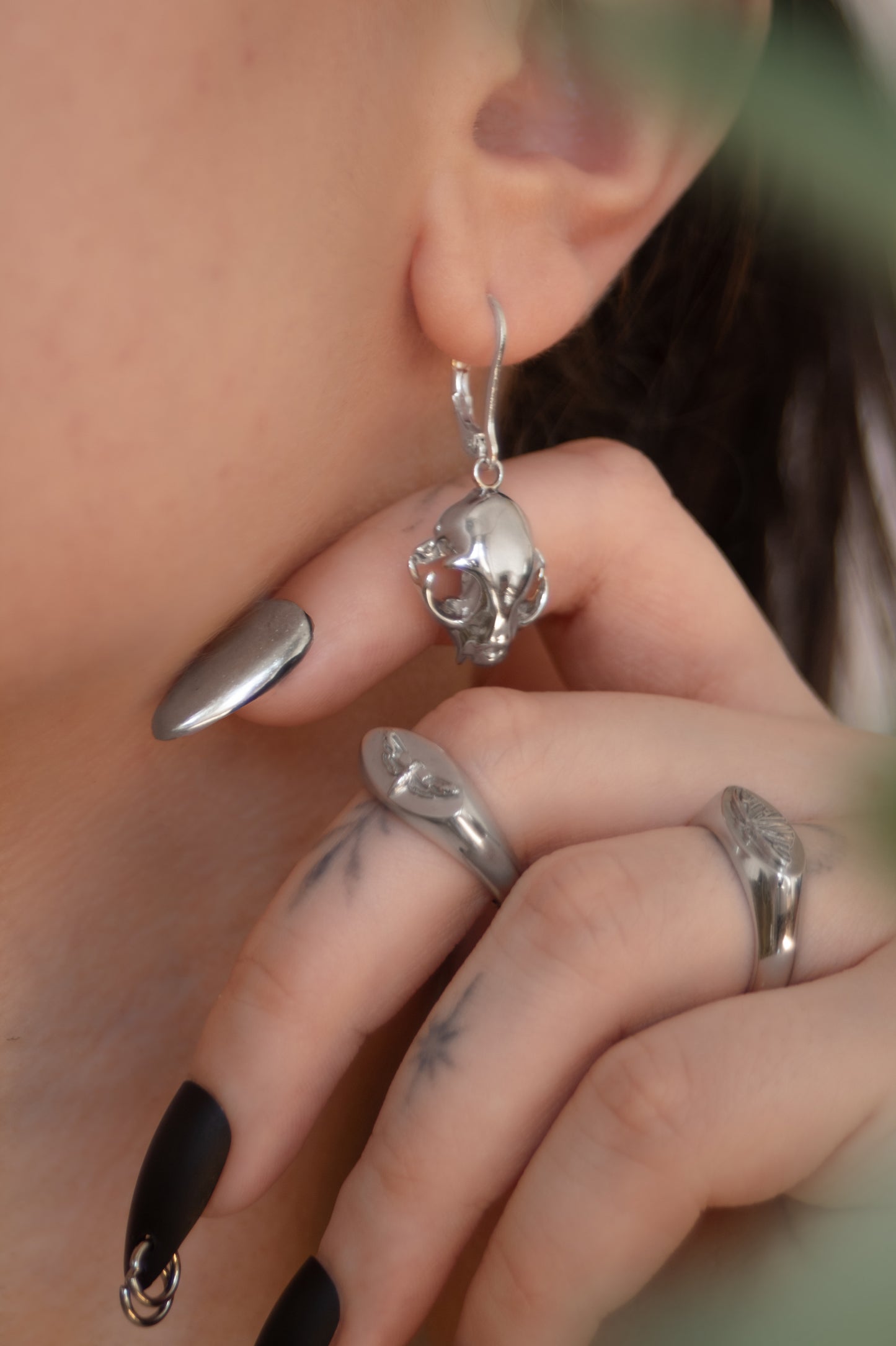 Side view of model wearing silver feline skull drop earrings, showing elegant dangle design and fit.