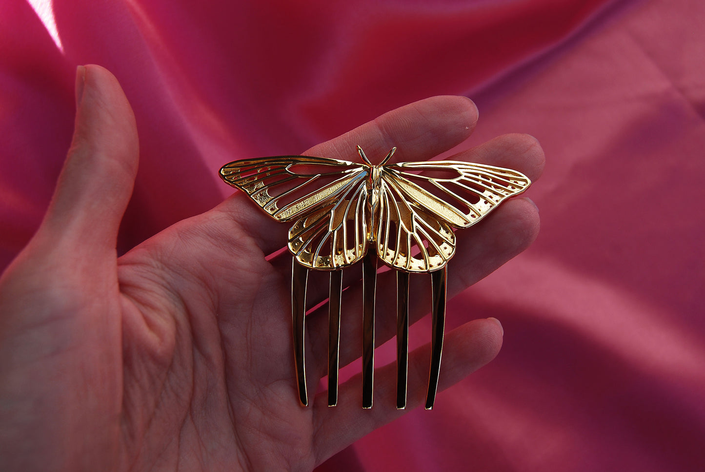Monarch Butterfly hair comb crafted in 14k gold plated brass, resting on a soft silk background. The delicate cut-out wings and luminous gold finish highlight the comb’s intricate design and luxurious craftsmanship.