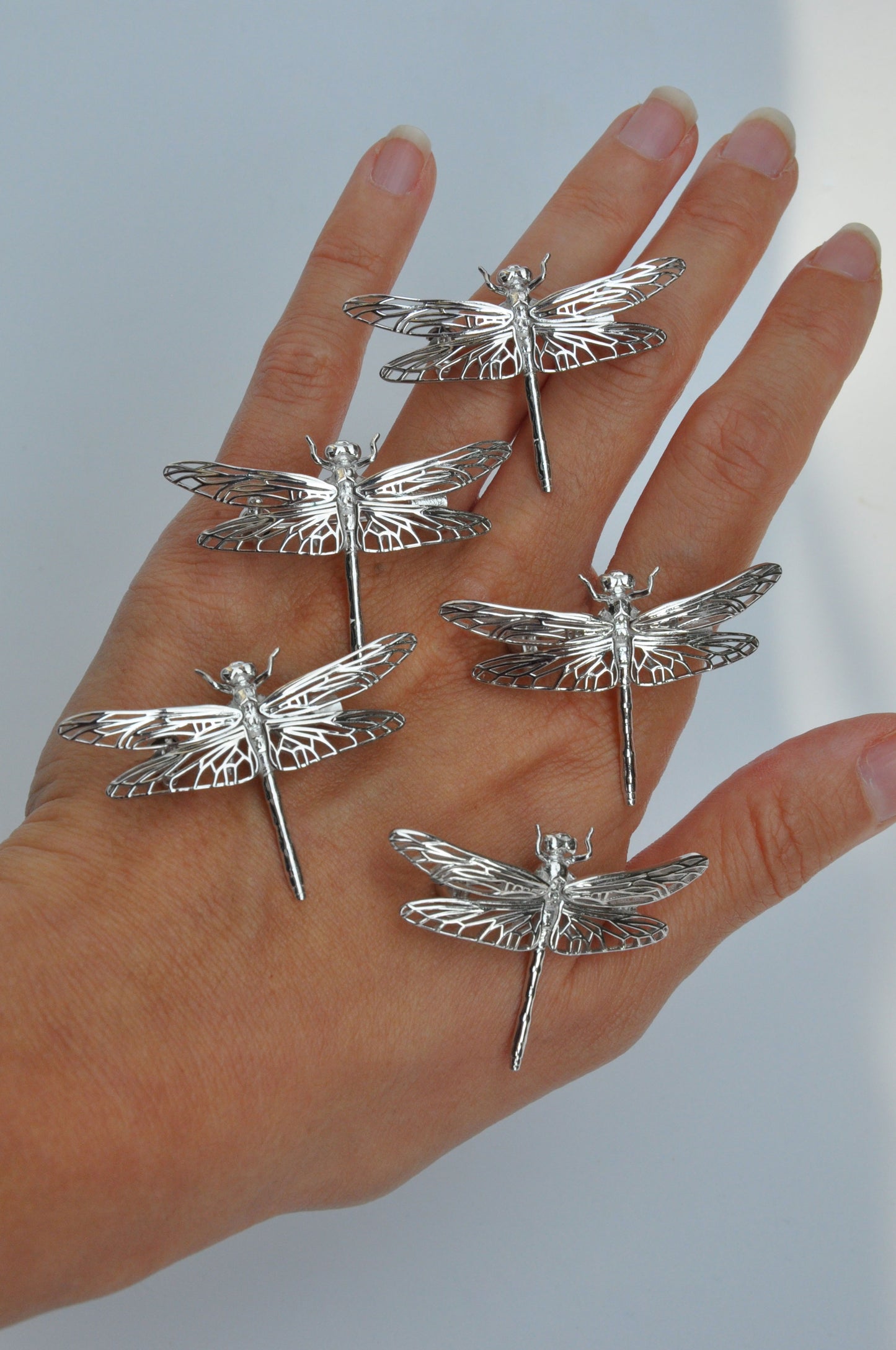 Several silver dragonfly brooches displayed in an open hand, showcasing variety in size and fine craftsmanship.