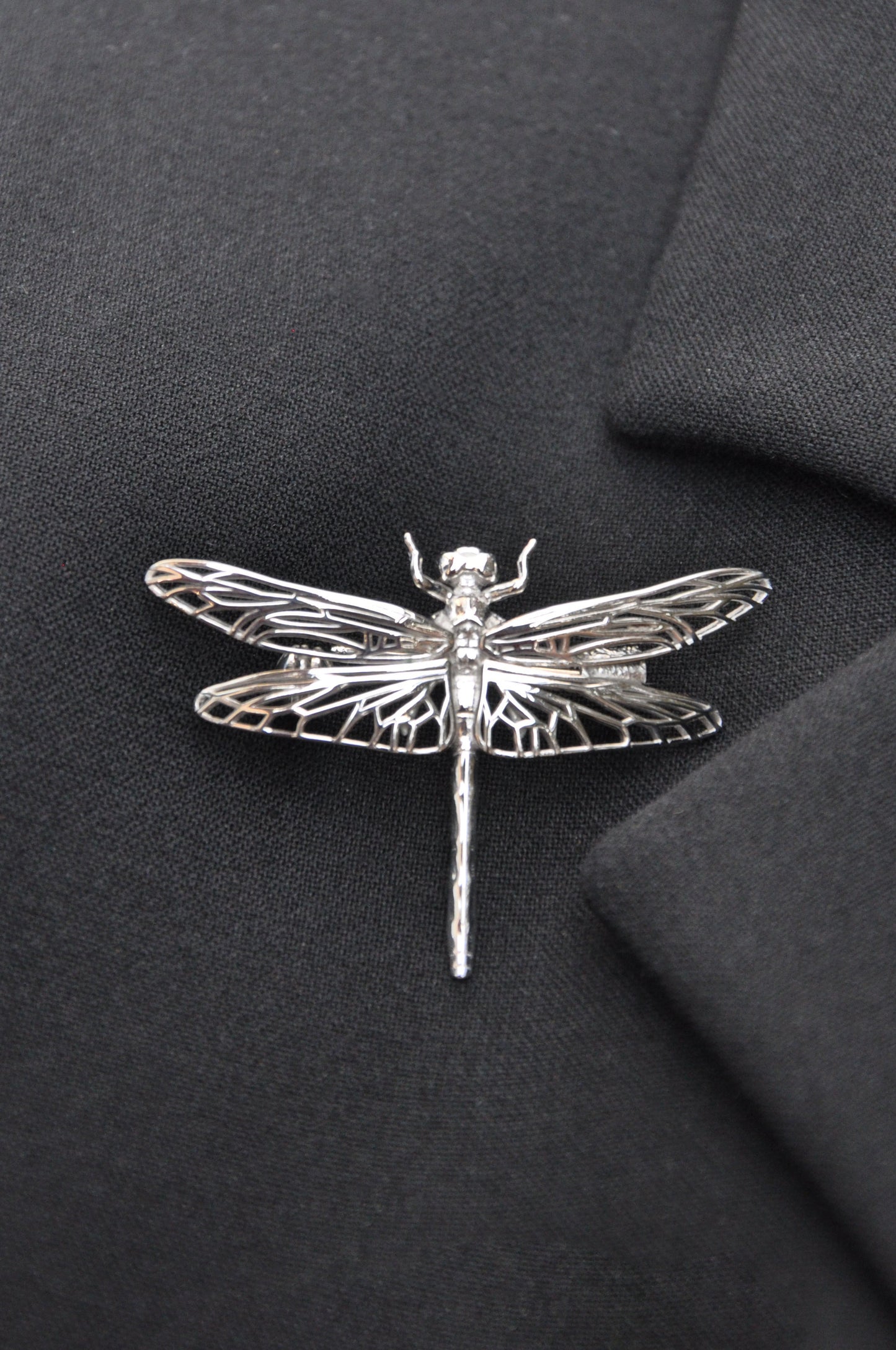 Silver dragonfly brooch pinned to black cloth, emphasizing the contrast and intricate nature-inspired design.