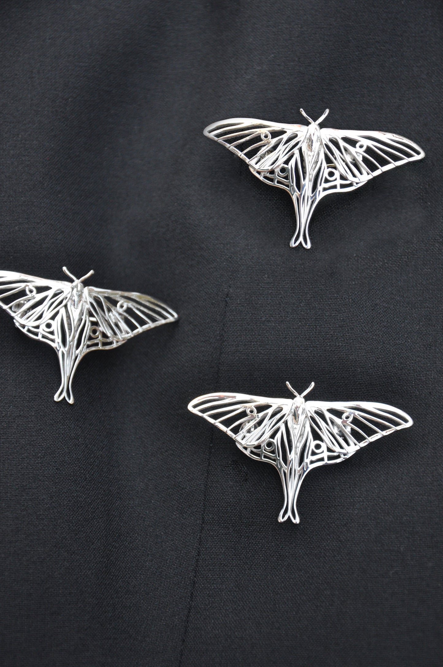 Silver Luna Moth brooch pinned on black cloth, emphasizing its shine and elegant insect-inspired design.