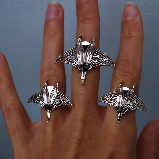 Hand wearing large and small sterling silver manta ray rings, showcasing ocean-inspired jewelry.