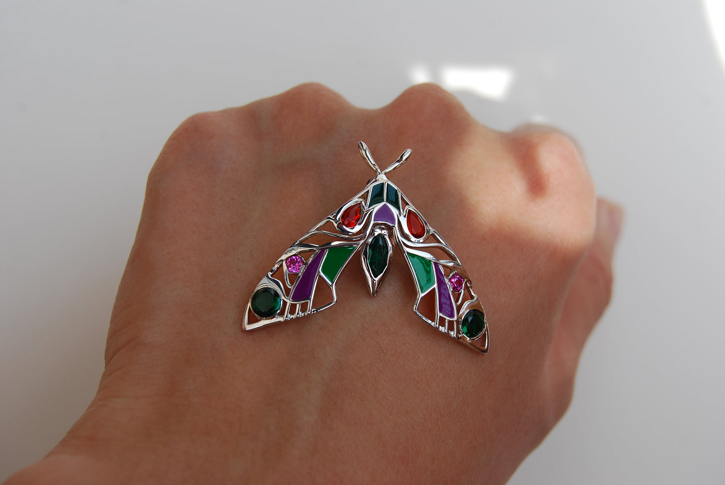 Close-up front view of silver moth pendant necklace on hand