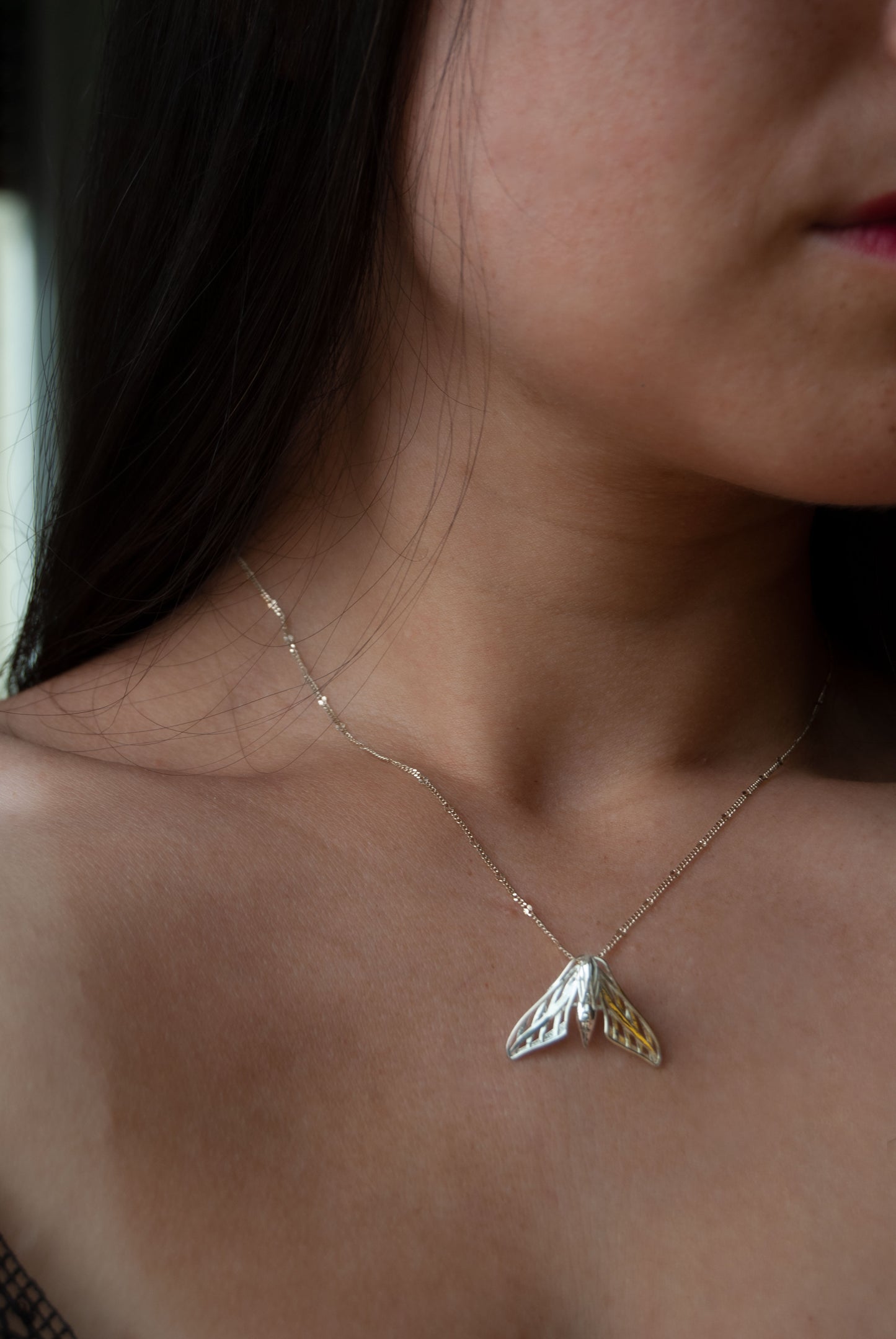 Model wearing a silver moth-shaped pendant