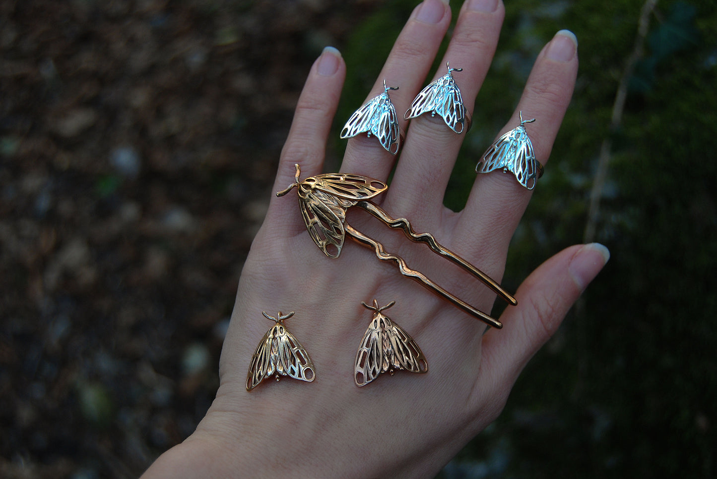 Bronze Tiger Moth hair pin displayed with silver Tiger Moth rings worn on the hand, showcasing handcrafted insect-inspired jewelry in mixed metallic finishes.