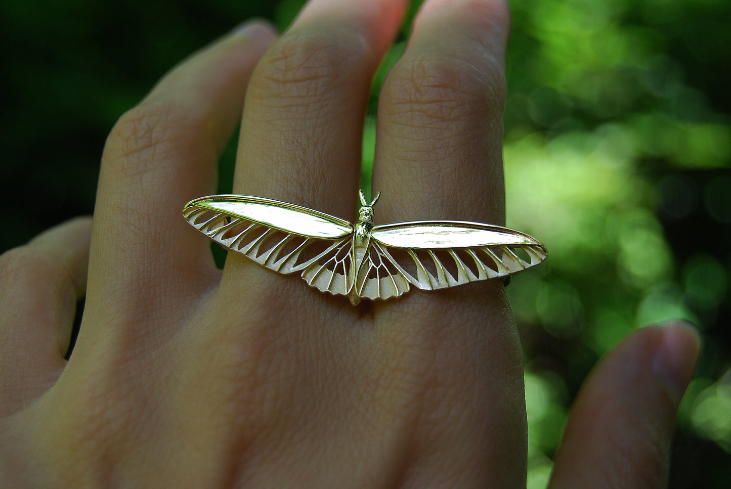Two Finger Gold butterfly ring on a person's finger with a blurred green background