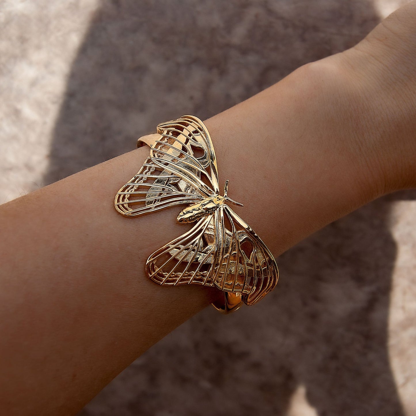 Front view of the Atlas Moth Bracelet in 14k gold-plated brass, worn by a model. The sculptural moth design wraps gracefully around the wrist, catching light with its polished gold finish. Styled with natural tones, the bracelet evokes elegance and a deep connection to nature.