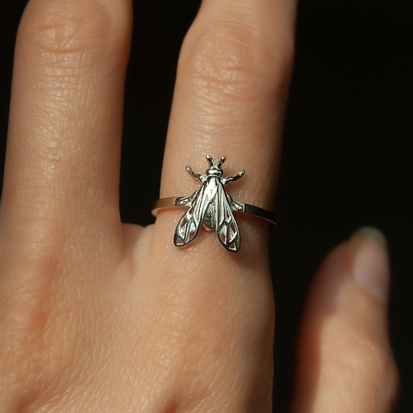 Handmade silver ring featuring a honeybee design on a rustic wooden background.