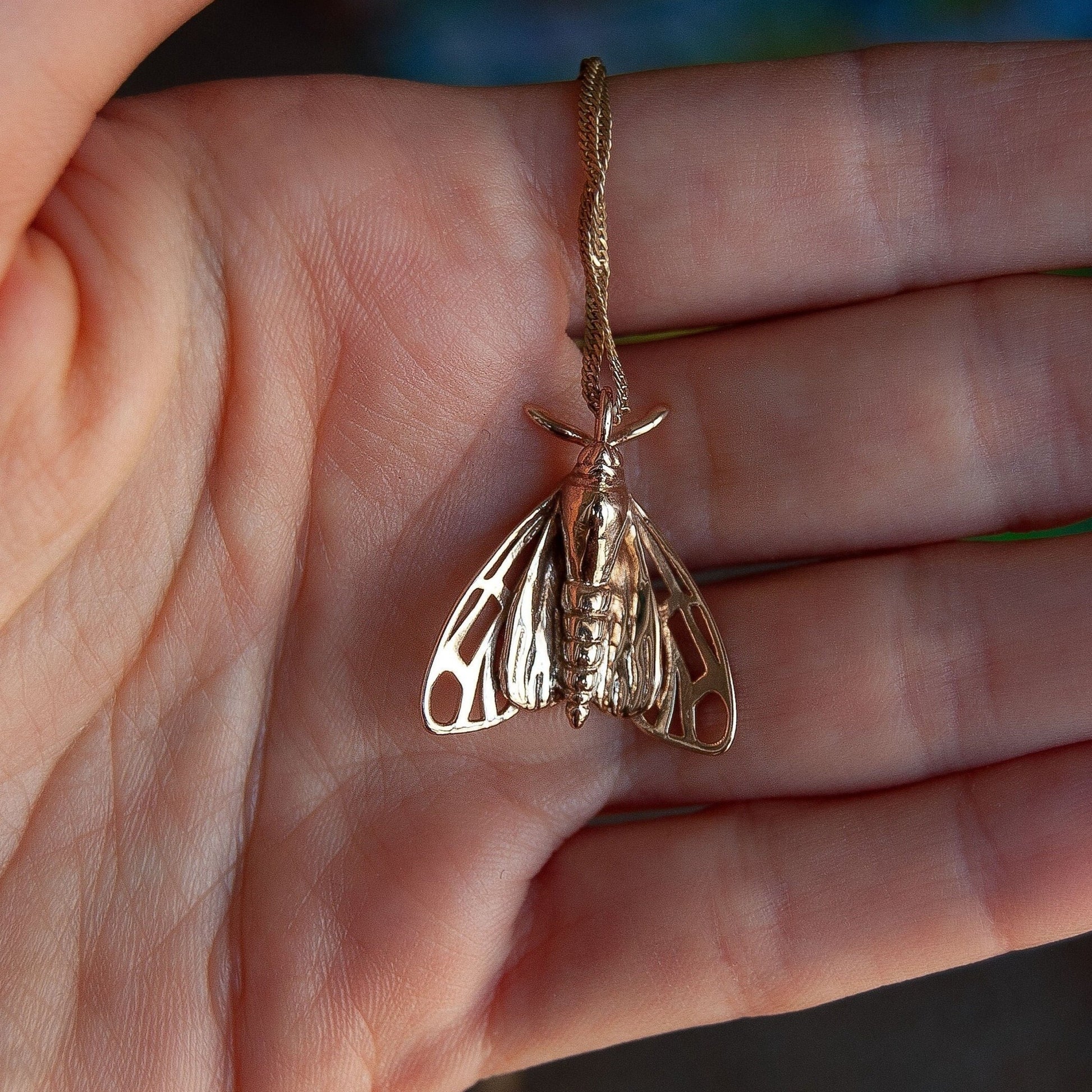 Back view of gold tiger moth pendant on hand, highlighting the detailed craftsmanship and form.