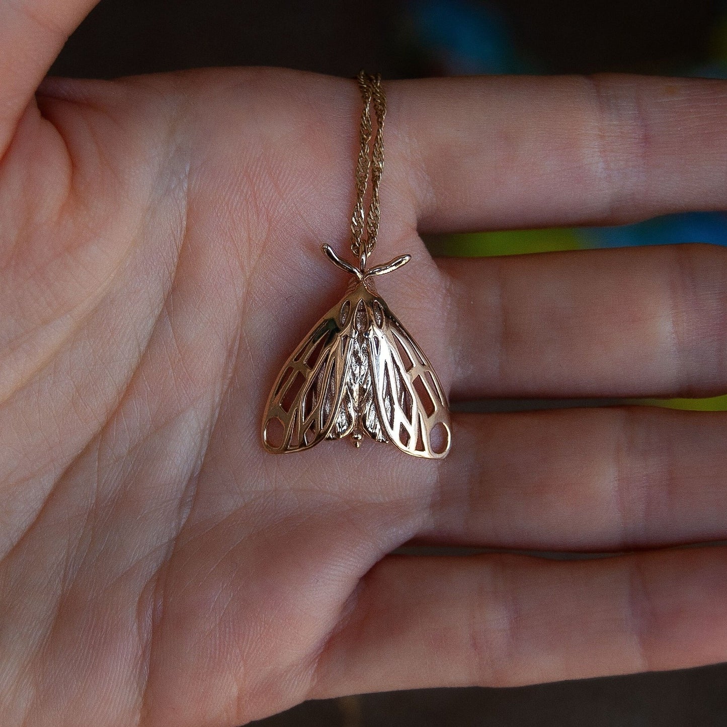 Alternative moth pendant in gold resting on hand, revealing winged insect jewelry design