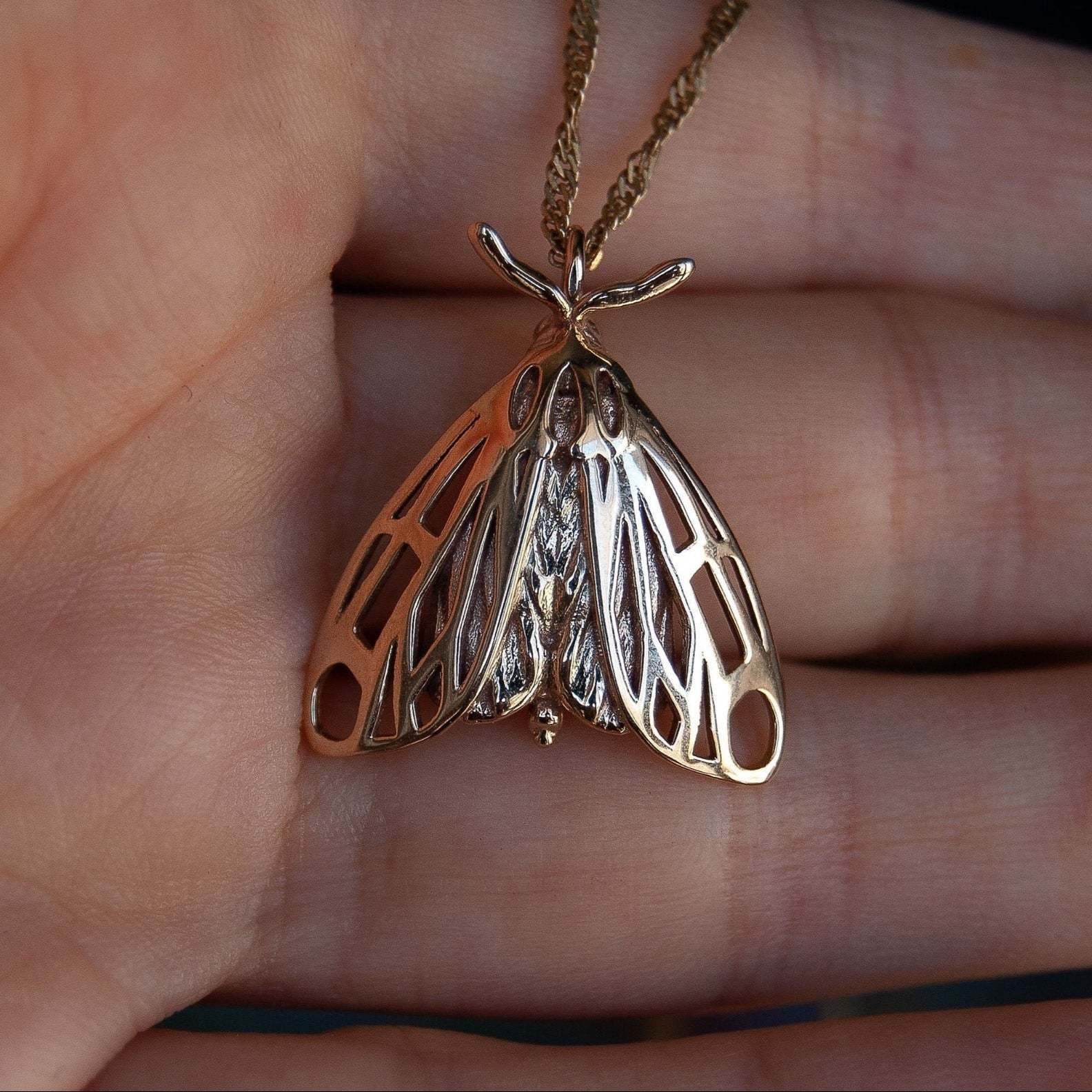 Alternative moth pendant in gold resting on hand, revealing winged insect jewelry design.