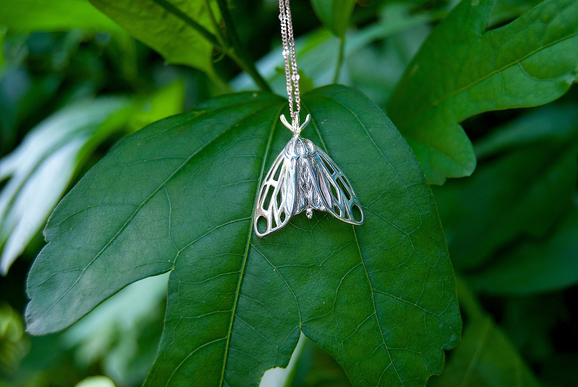 Silver tiger moth jewelry placed outdoors in natural surroundings, emphasizing its nature inspired necklace style.