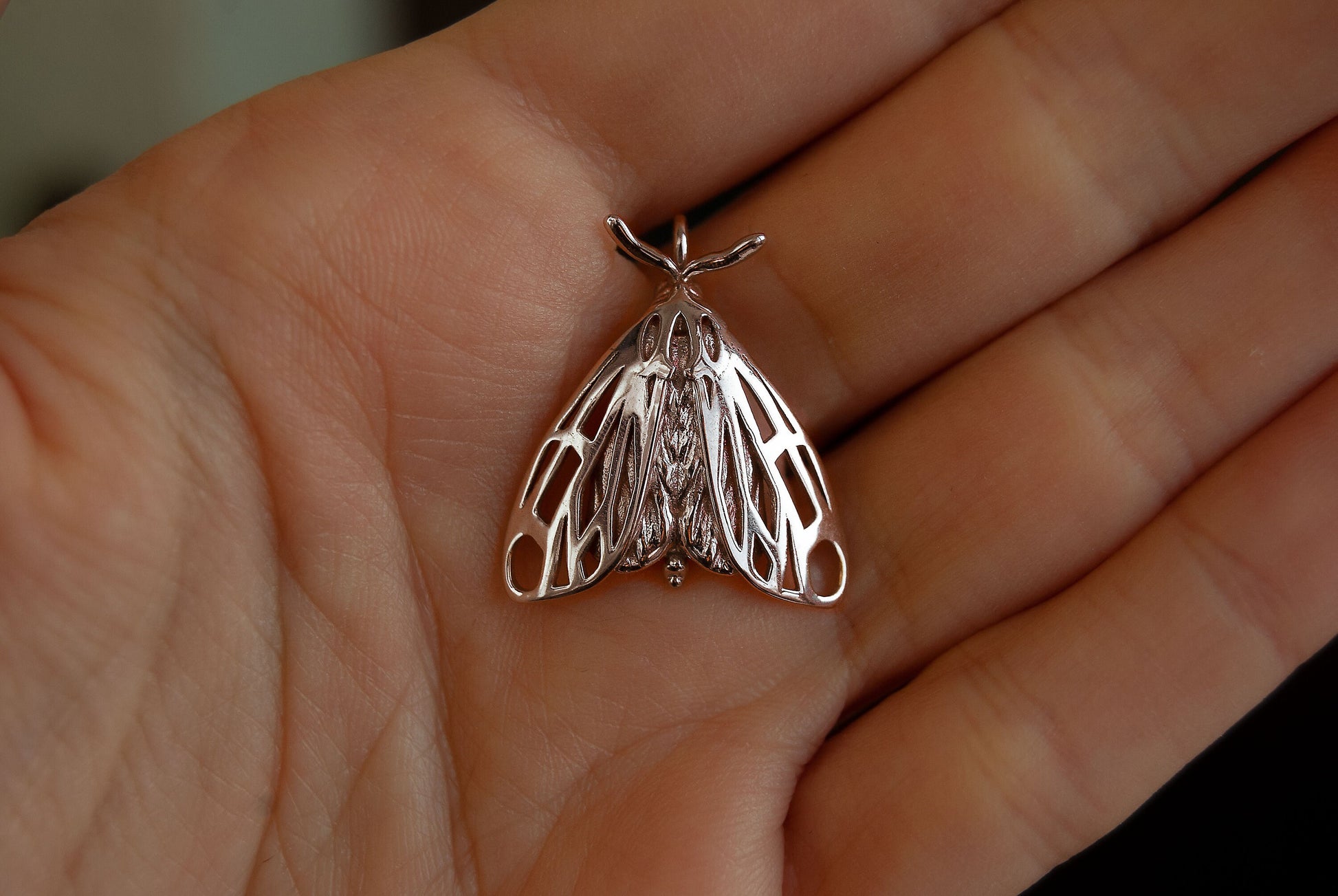 Sterling silver moth charm worn on hand, highlighting the fine craftsmanship of this tiger moth pendant.