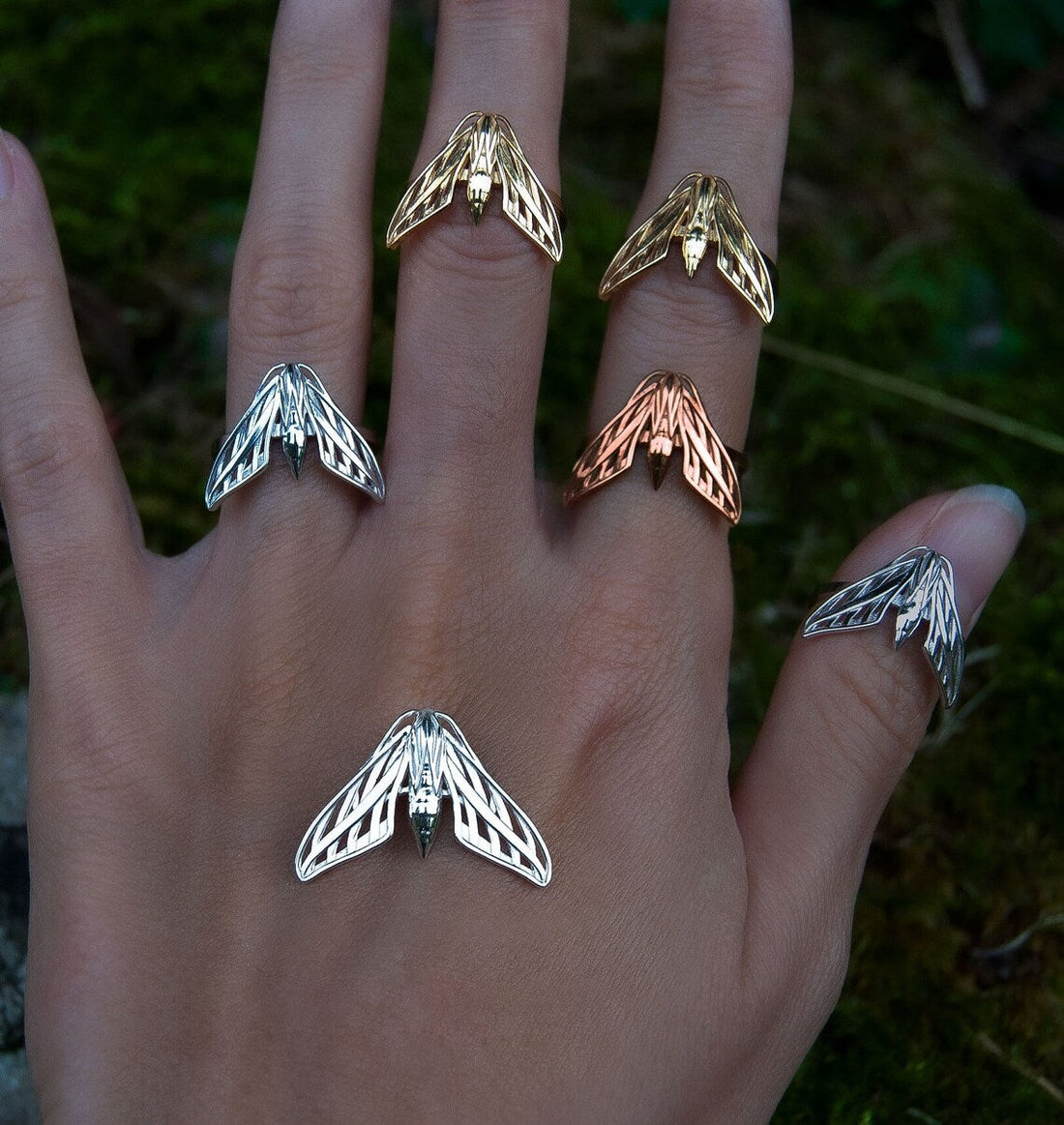 Hand wearing Sphinx Moth rings and holding matching pendants, showcasing detailed silver jewelry inspired by nocturnal moths.