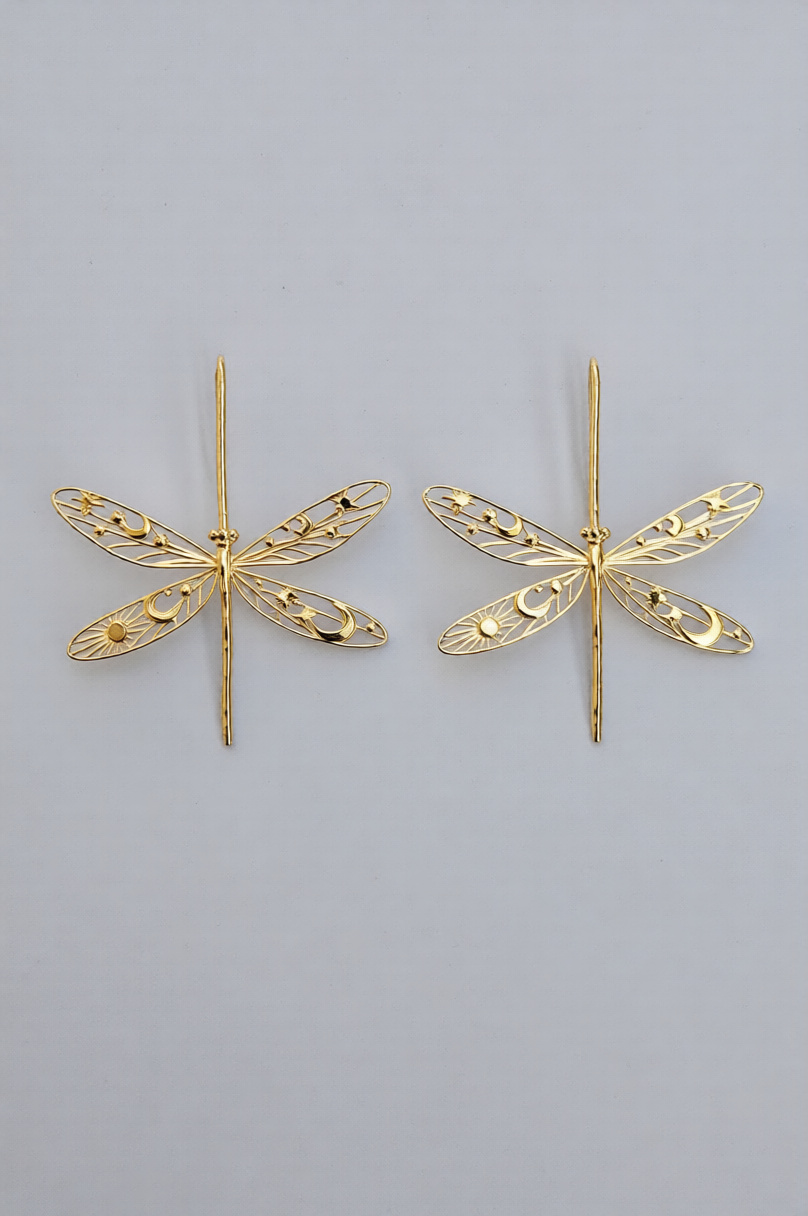Gold damselfly earrings with intricate celestial cut‑out wings featuring stars, moons, and sun motifs