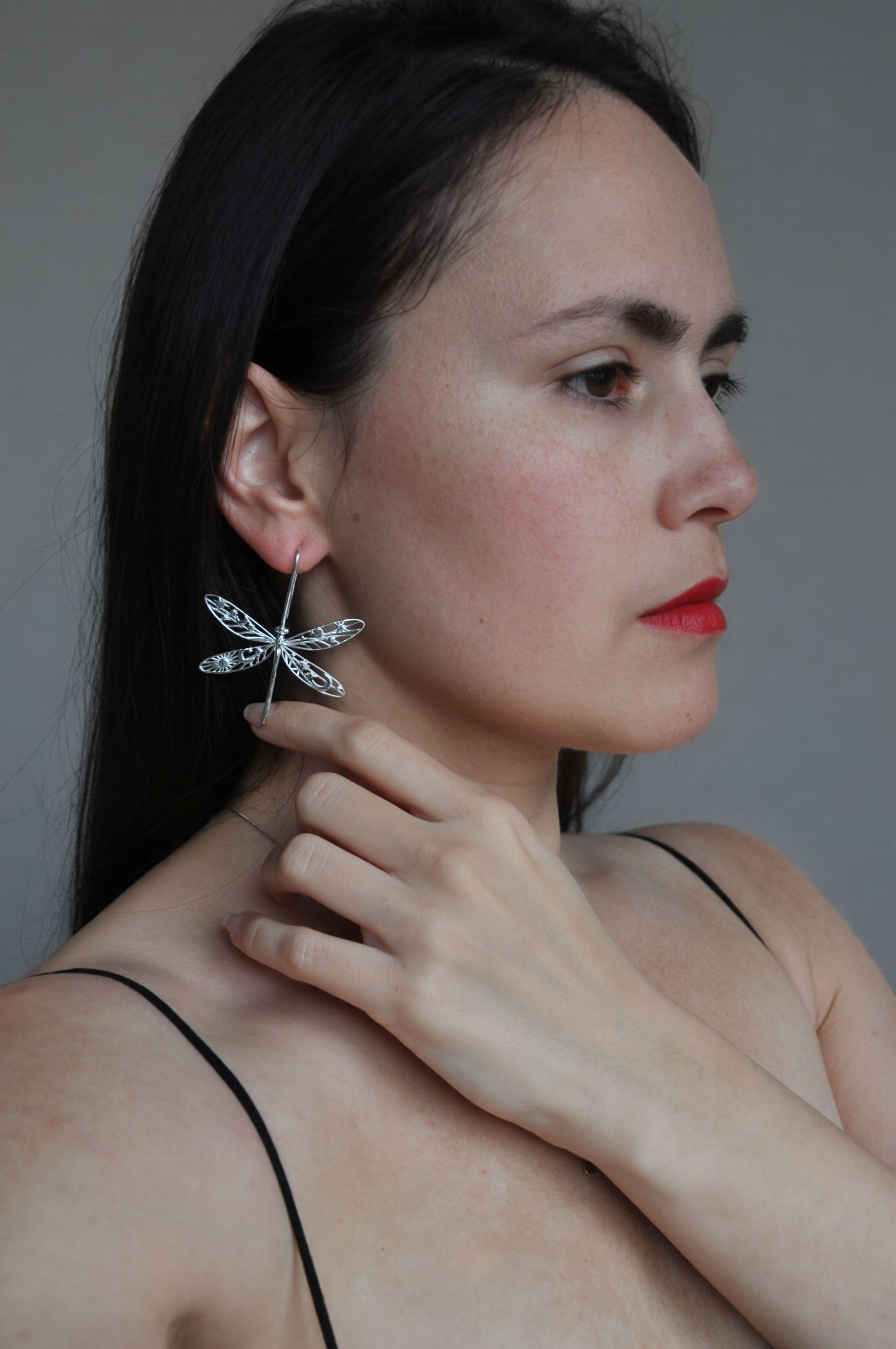 Woman wearing a gold damselfly earring with detailed celestial wing cut‑outs, shown in a close‑up side profile.