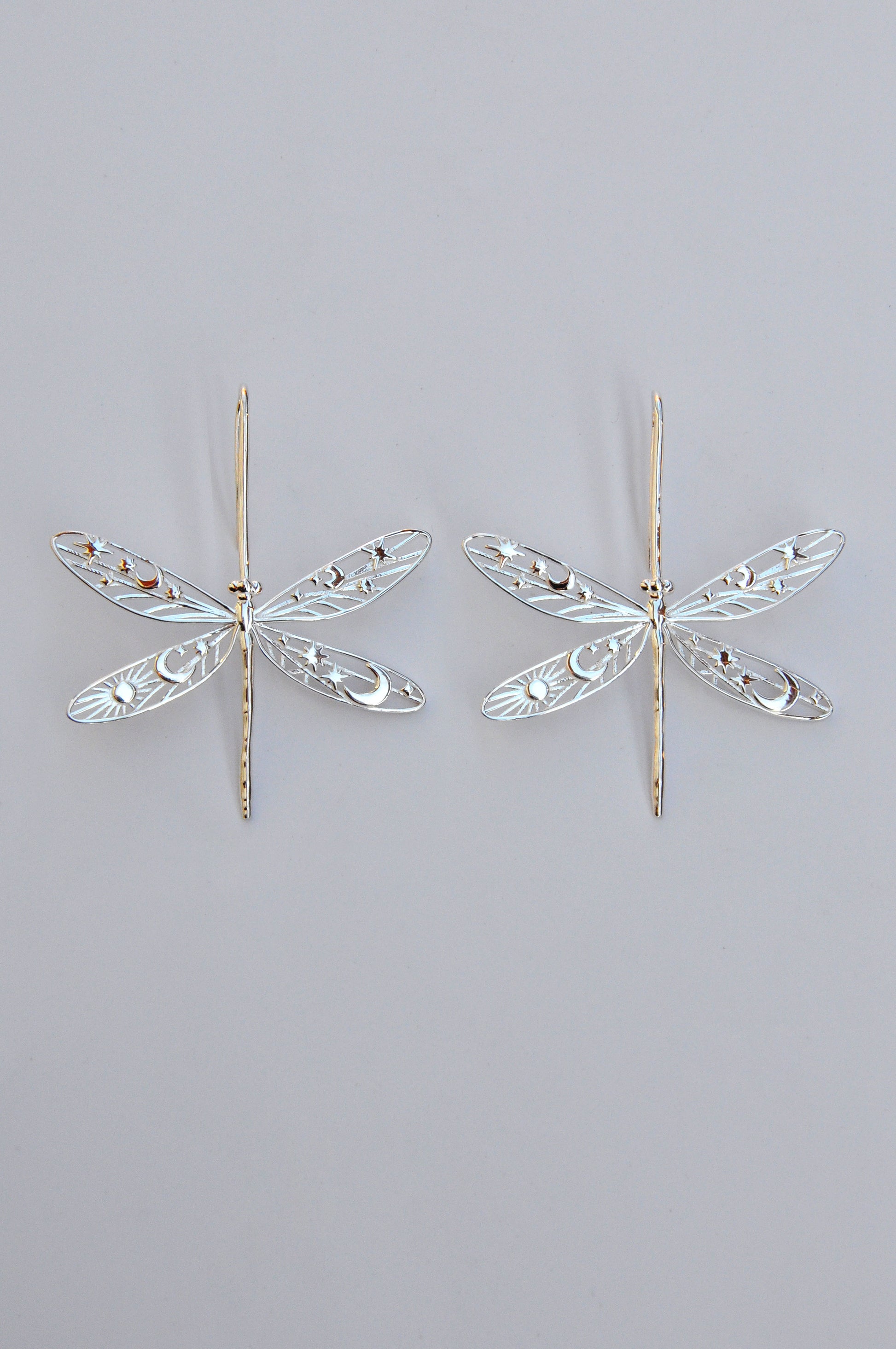 Gold damselfly earrings with intricate celestial cut‑out wings featuring stars, moons, and sun motifs
