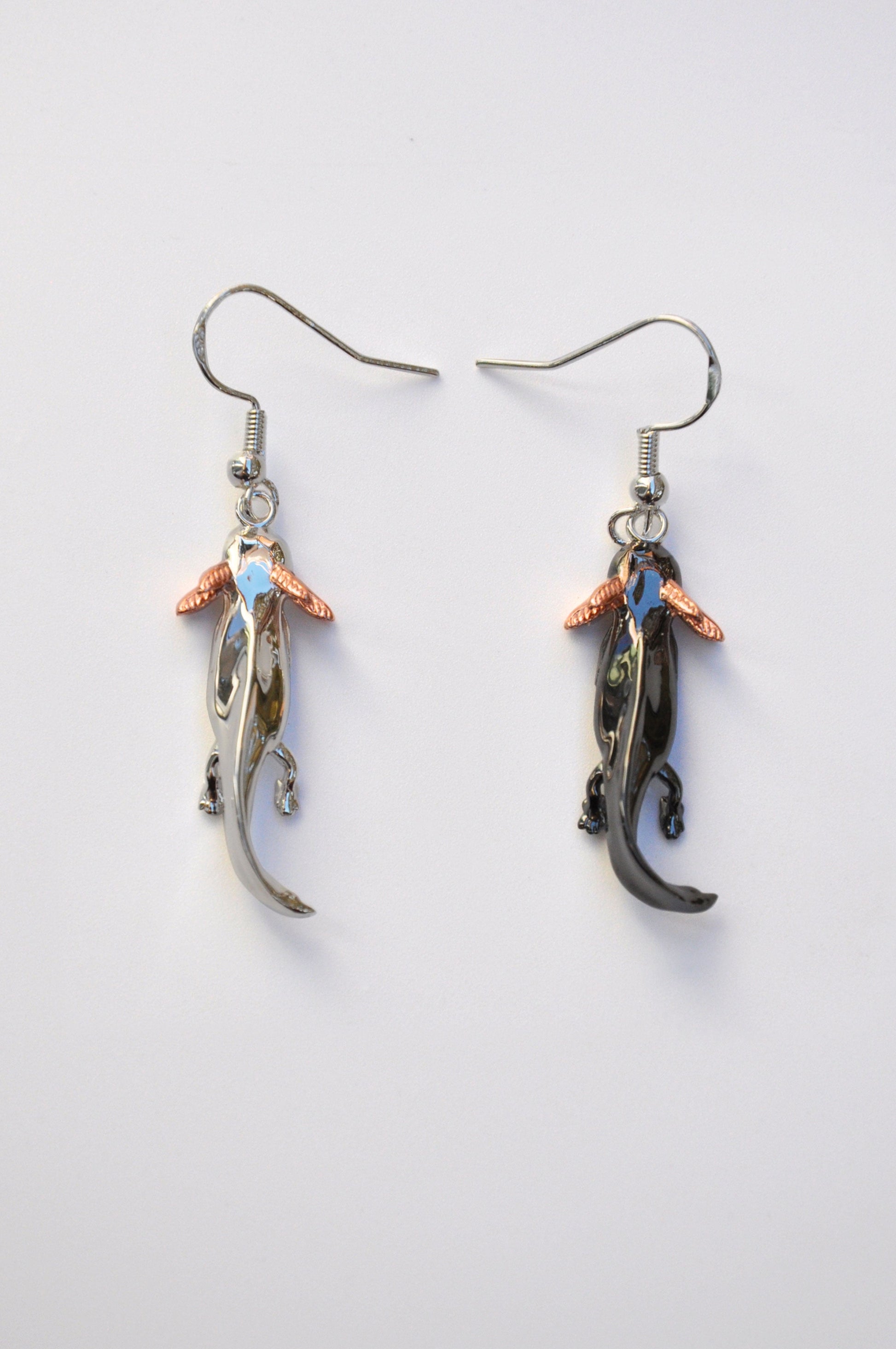 Front view of the mismatched Axolotl Drop Earrings on a white background — one in sterling silver, the other in black rhodium-plated silver, both with rose gold-plated gills.