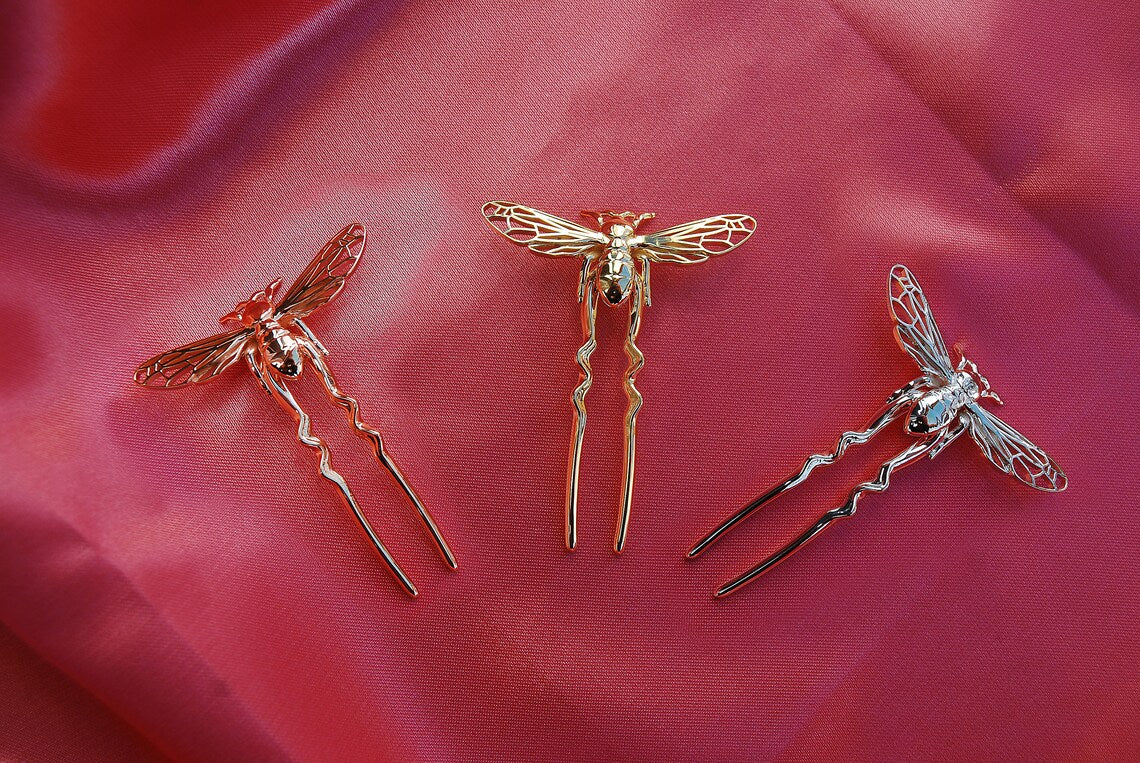 Rose gold, silver, and gold bee hair pins arranged on soft silk fabric, showcasing handcrafted insect-inspired jewelry in elegant metallic finishes.