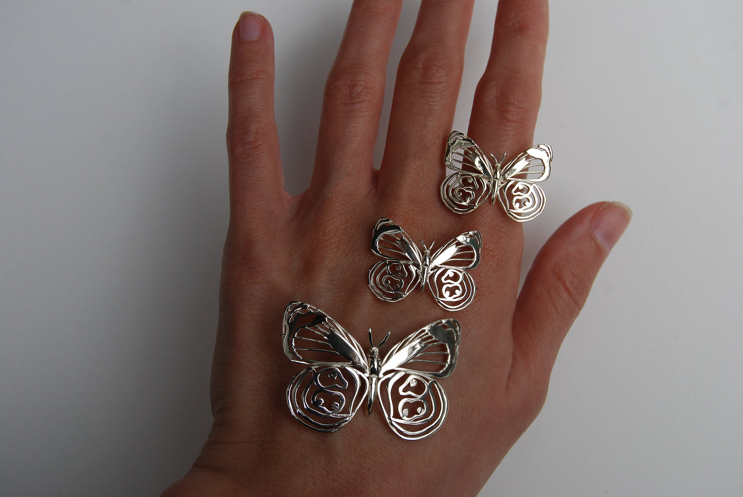 Butterfly rings and pendant worn on hand in outdoor setting, showcasing nature-themed jewelry collection.