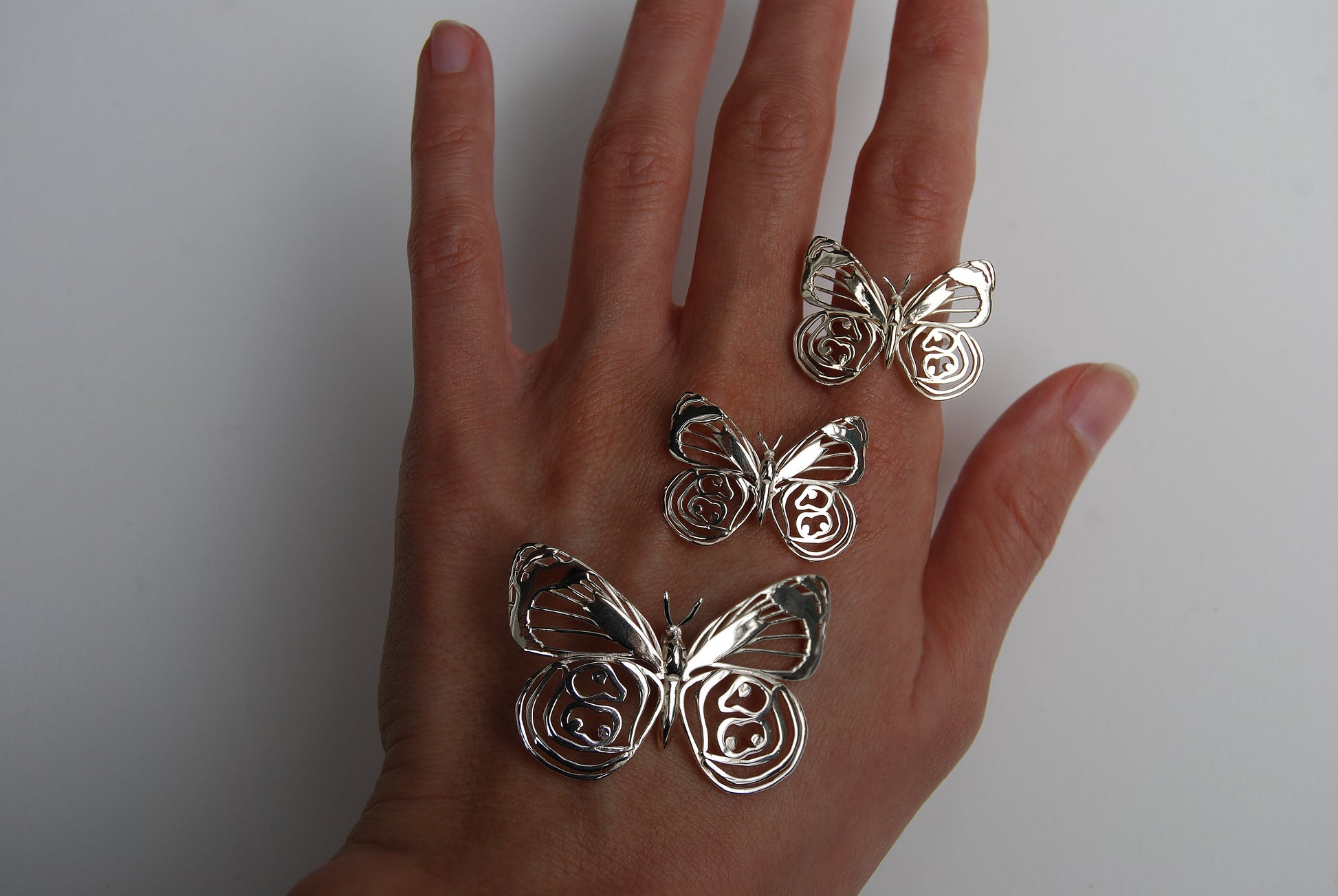 Butterfly rings and pendant worn on hand in outdoor setting, showcasing nature-themed jewelry collection.