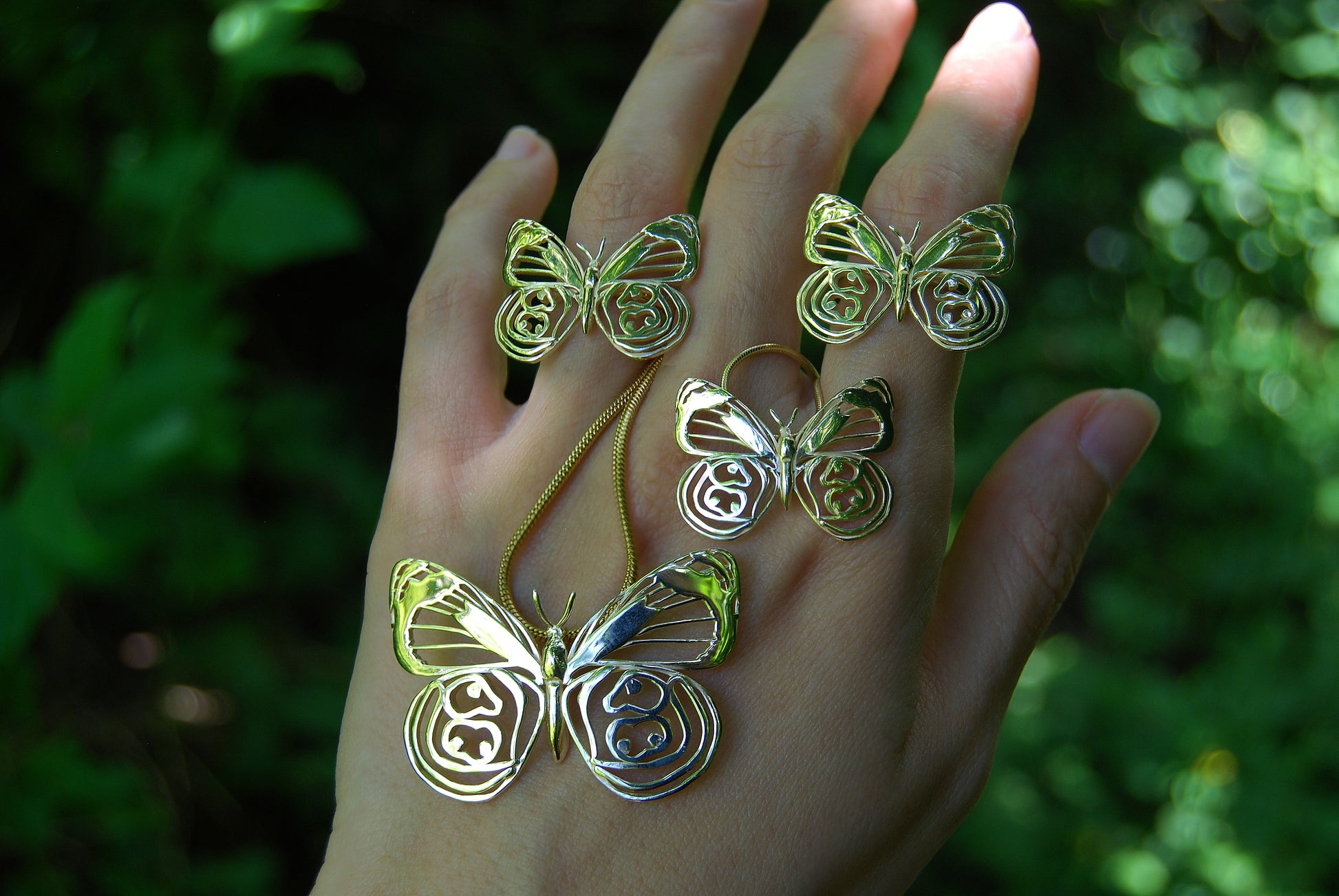 Butterfly ring and matching pendant worn on hand in natural setting, emphasizing organic beauty and forest-inspired jewelry.
