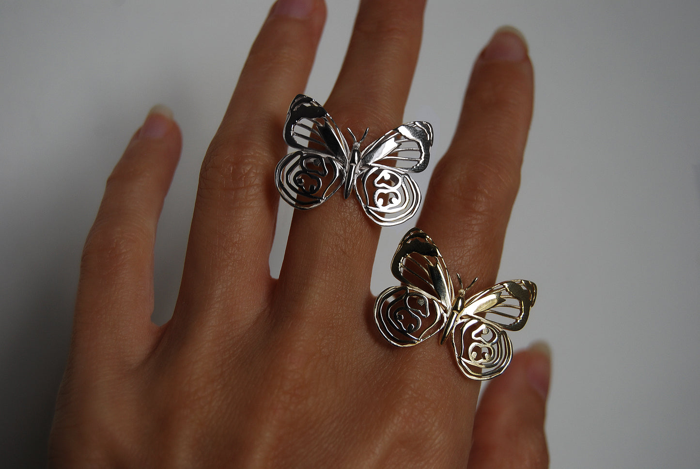 Two butterfly rings displayed on hand, each with unique wing design and handcrafted detail.