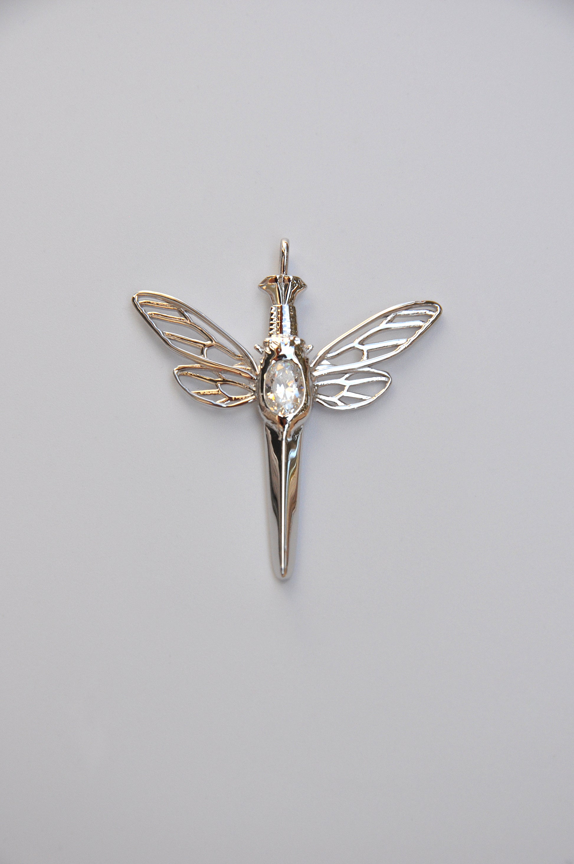 Intricate cicada perched on a silver dagger pendant with white stone, a talisman of quiet power and elegance
