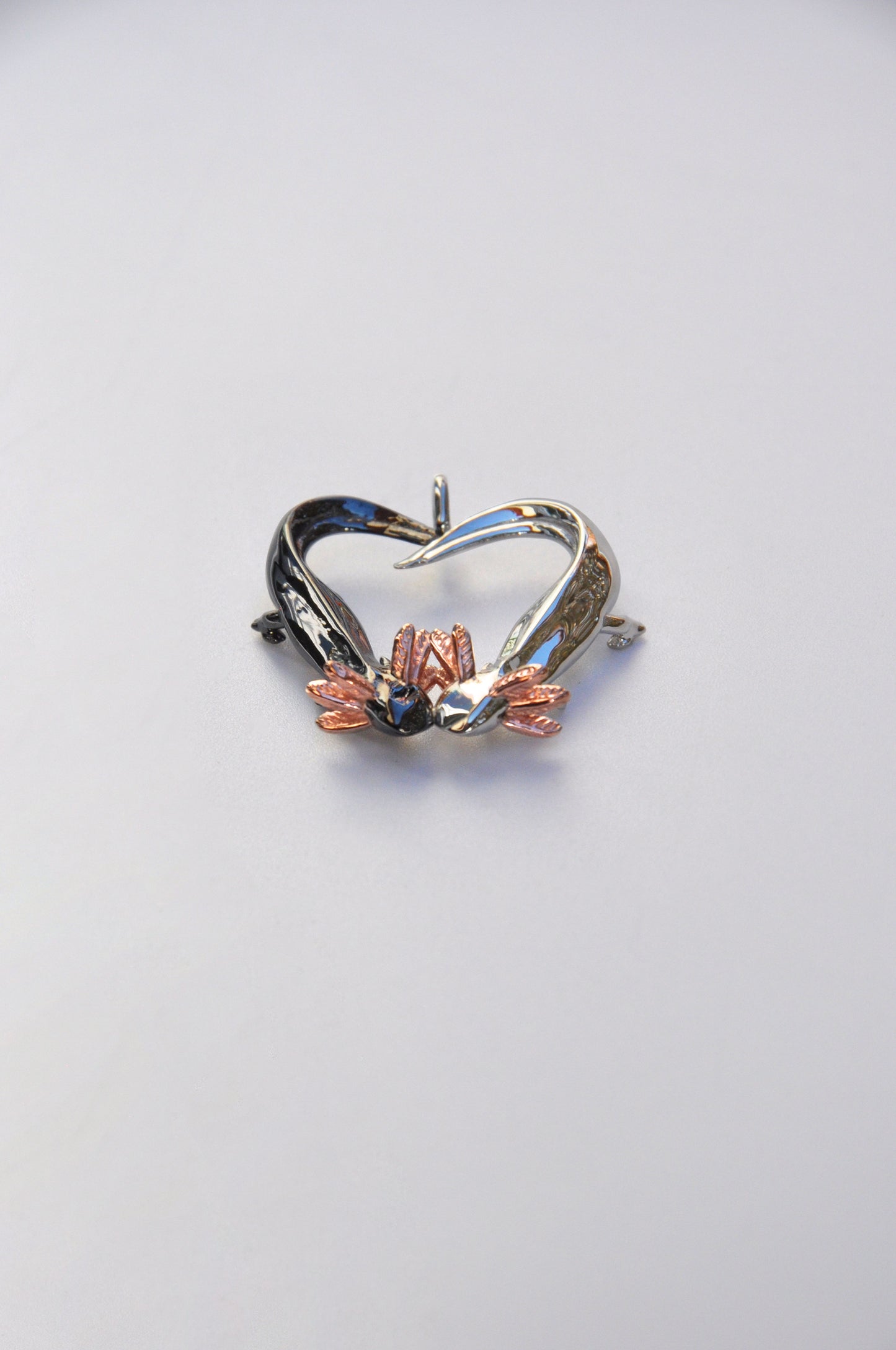 Bottom view of the Exolotl Love Pendant on a white background, showing the intertwined tails and sculptural symmetry.