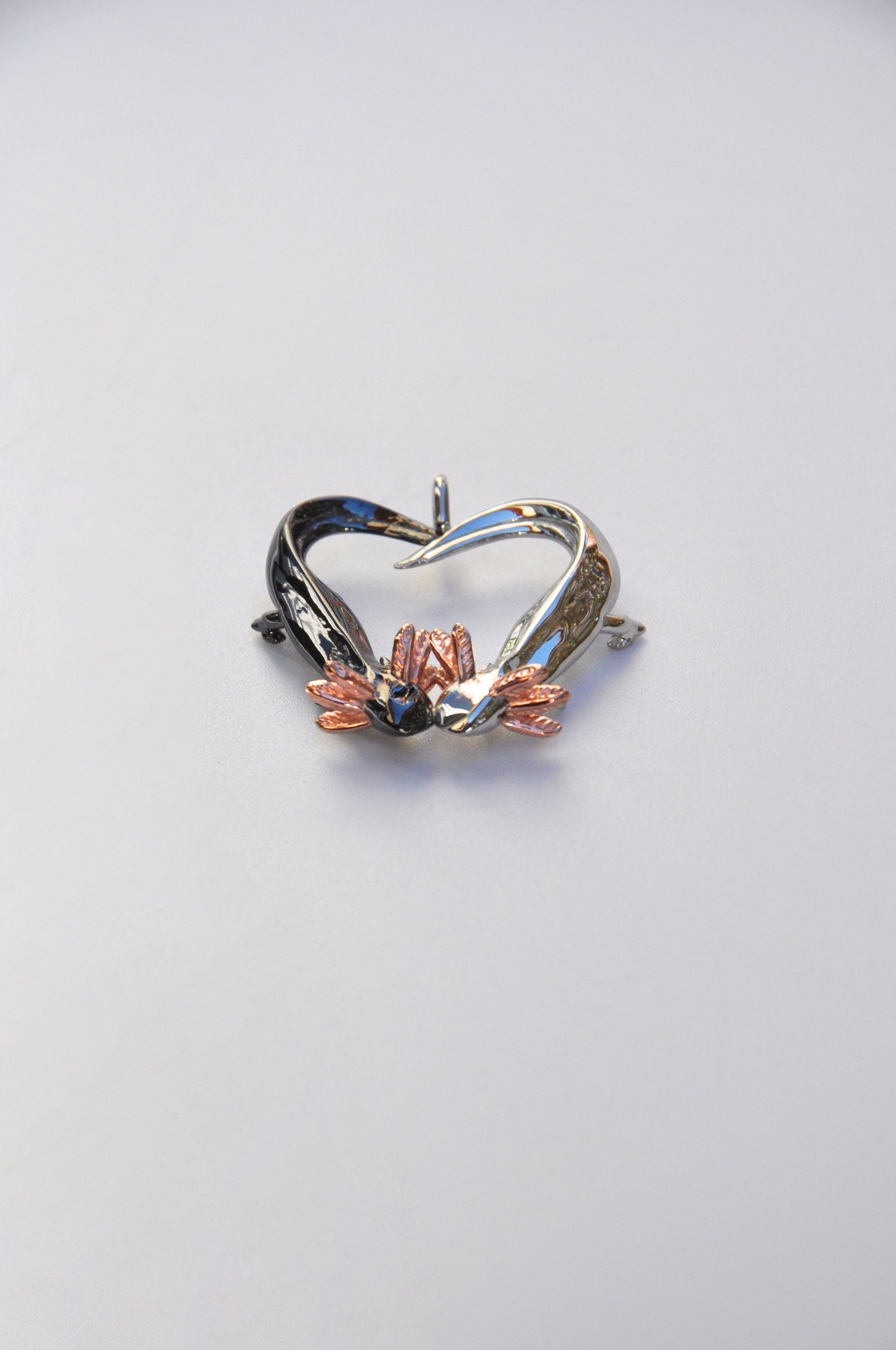 Bottom view of the Exolotl Love Pendant on a white background, showing the intertwined tails and sculptural symmetry.