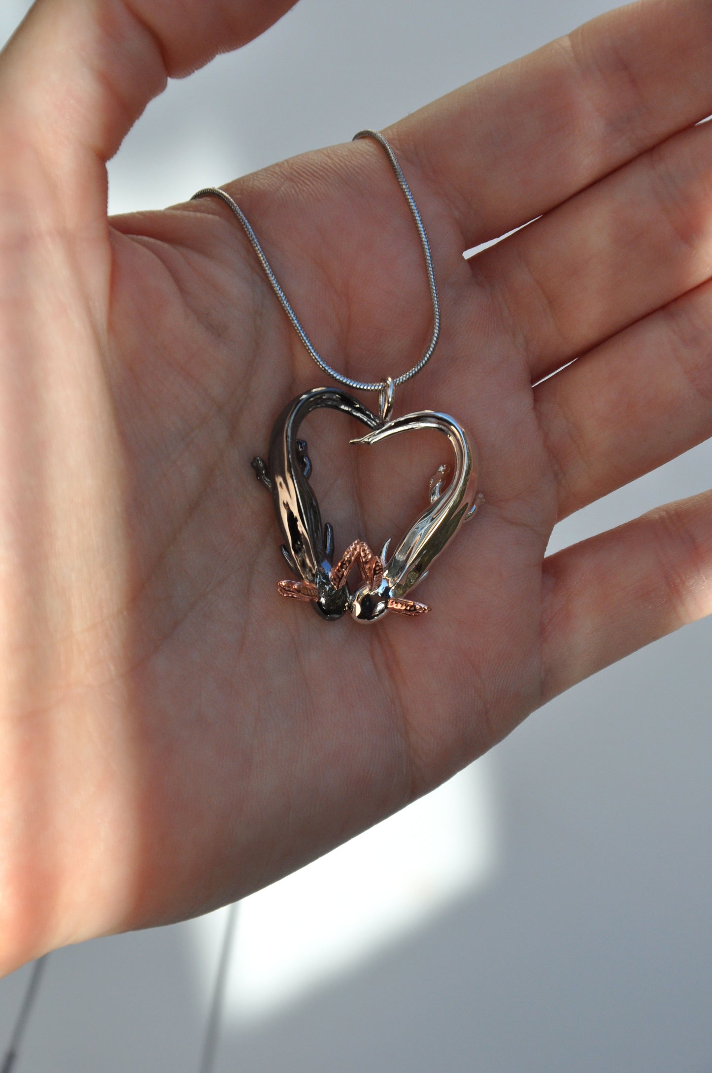 Front-facing view of the pendant held in hand, emphasizing the heart shape and rose gold-plated gills.