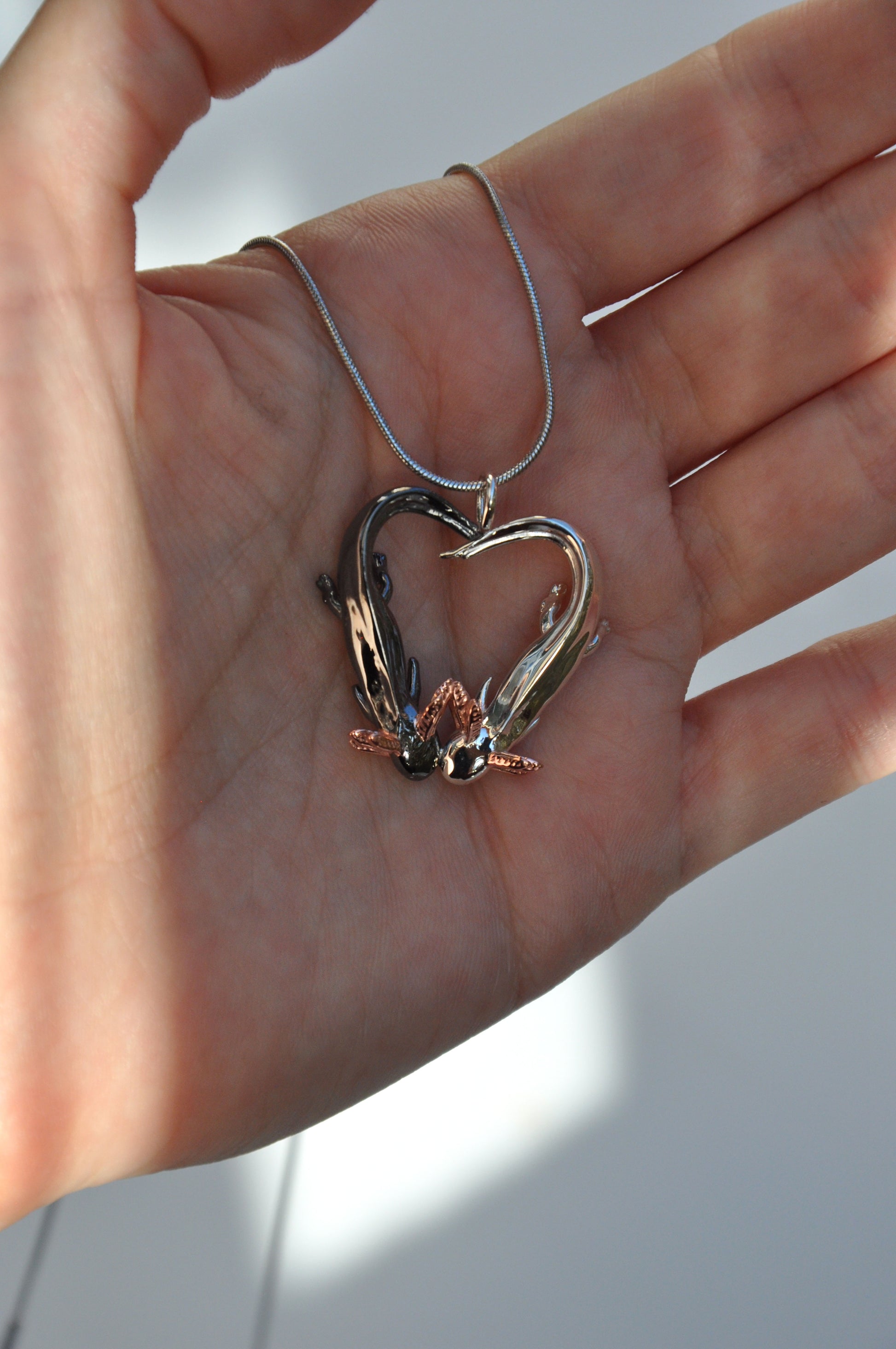 Front-facing view of the pendant held in hand, emphasizing the heart shape and rose gold-plated gills.