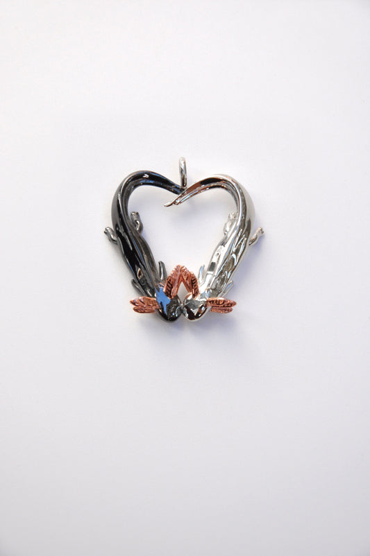 Front view of the Exolotl Love Pendant on a white background, showing two axolotls forming a heart with intertwined tails — one in polished silver, the other in black rhodium.