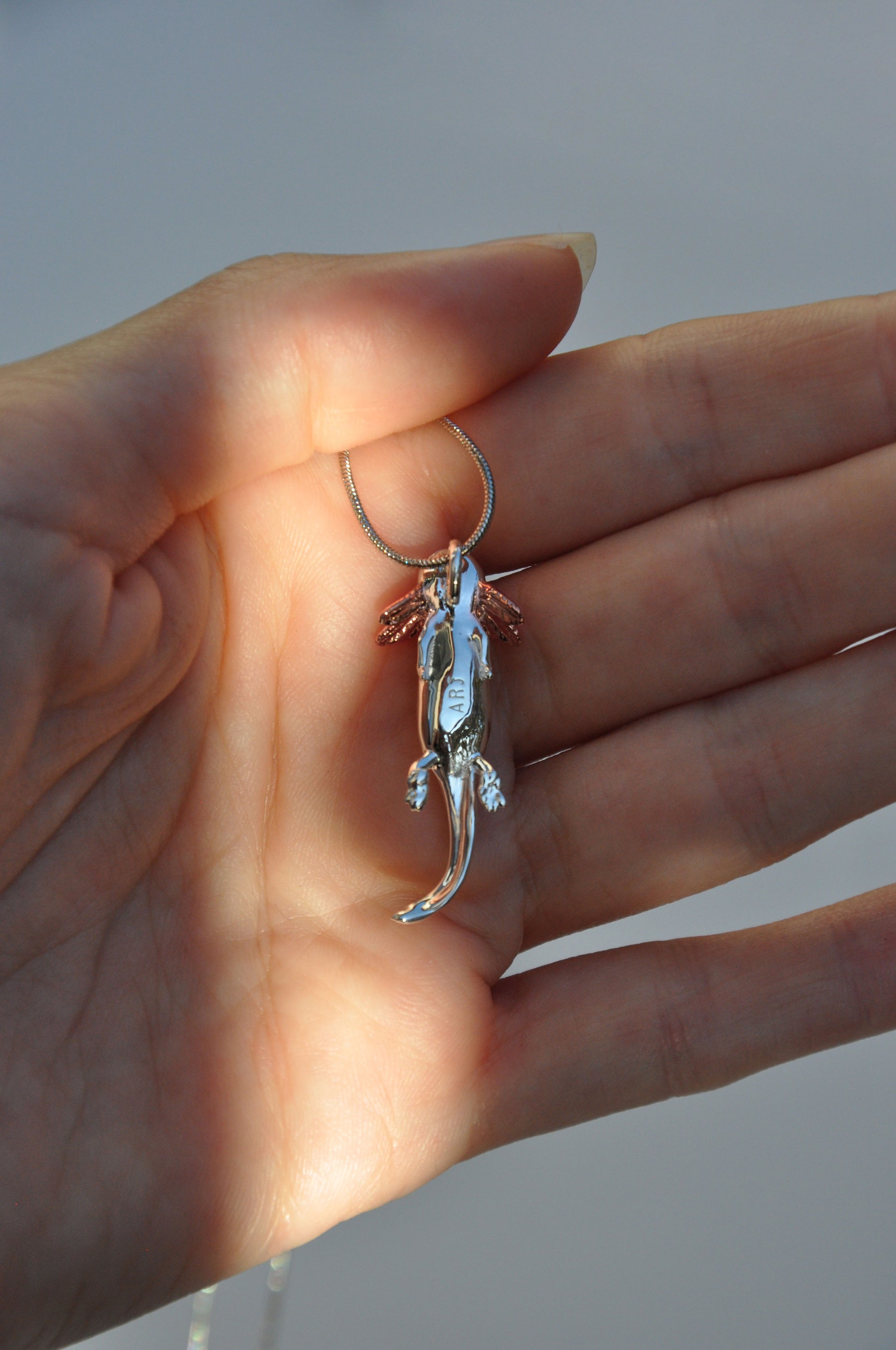 Back side of the Exolotl pendant held in hand, revealing its sculpted details and smooth finish.