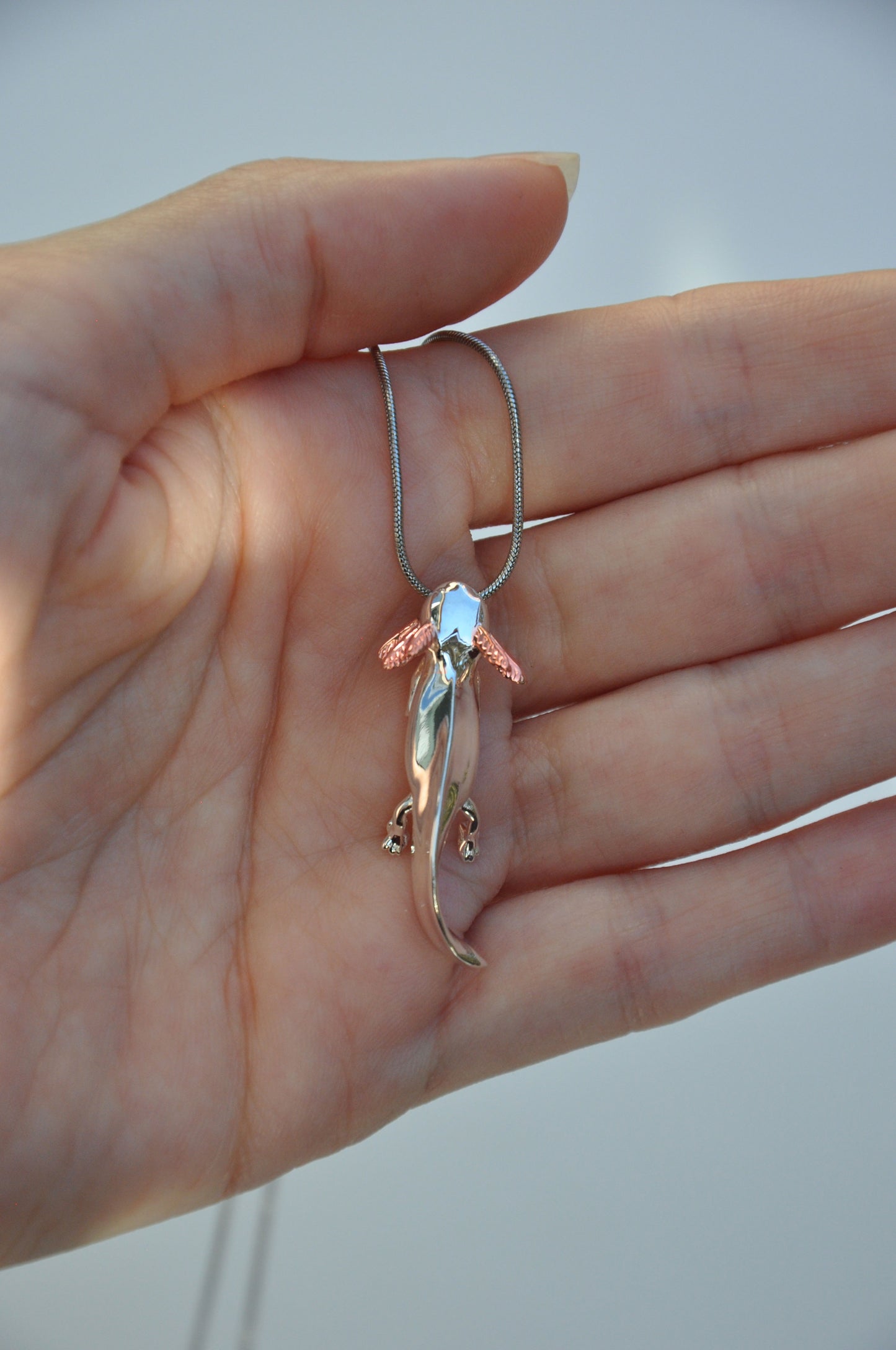 Close-up of the Exolotl pendant held in hand, highlighting its expressive face and rose gold accents.