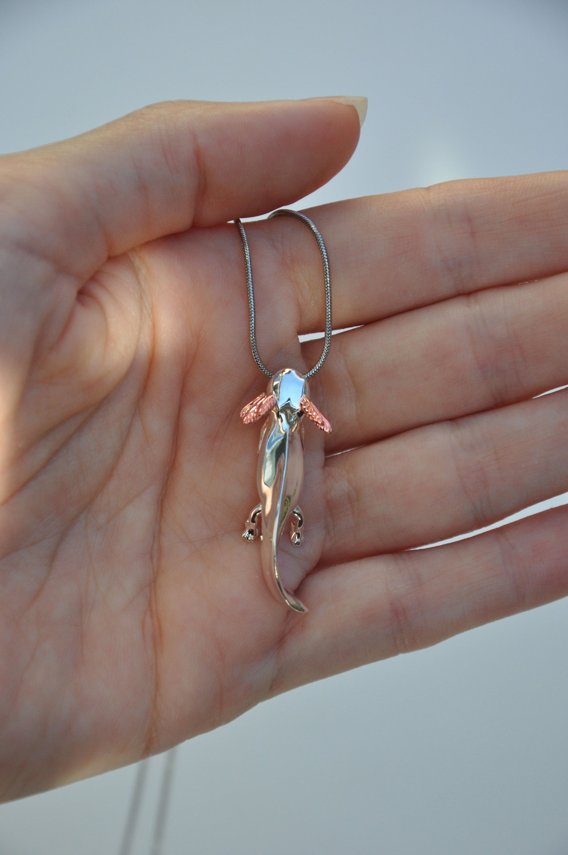 Close-up of the Exolotl pendant held in hand, highlighting its expressive face and rose gold accents.