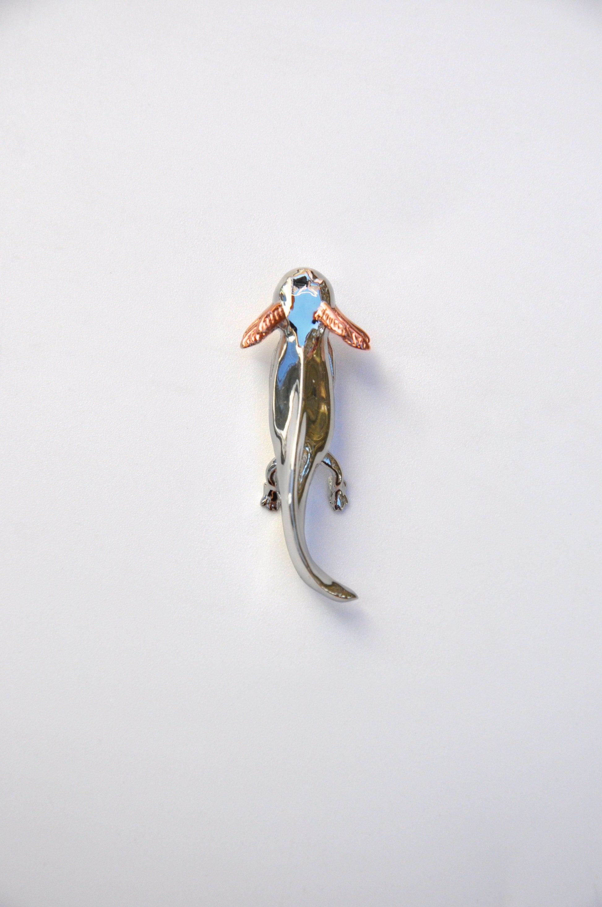 Front view of the handcrafted Exolotl pendant on a white background, showing its sterling silver body and rose gold-plated gills.
