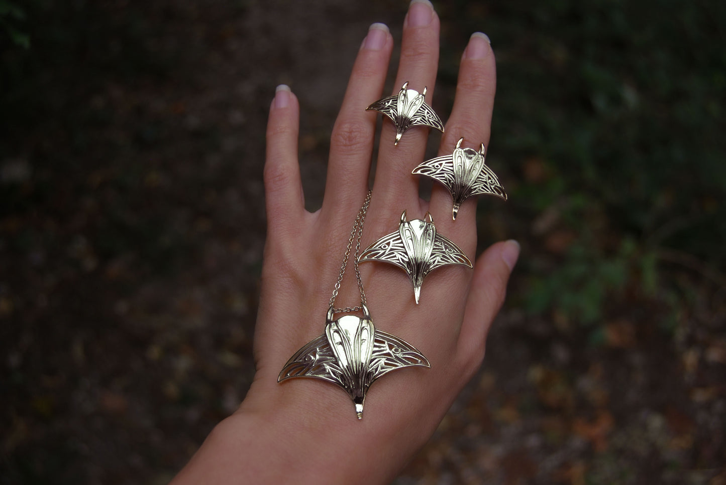 Hand wearing gold manta ray pendant and matching ring, featuring handcrafted ocean jewelry.