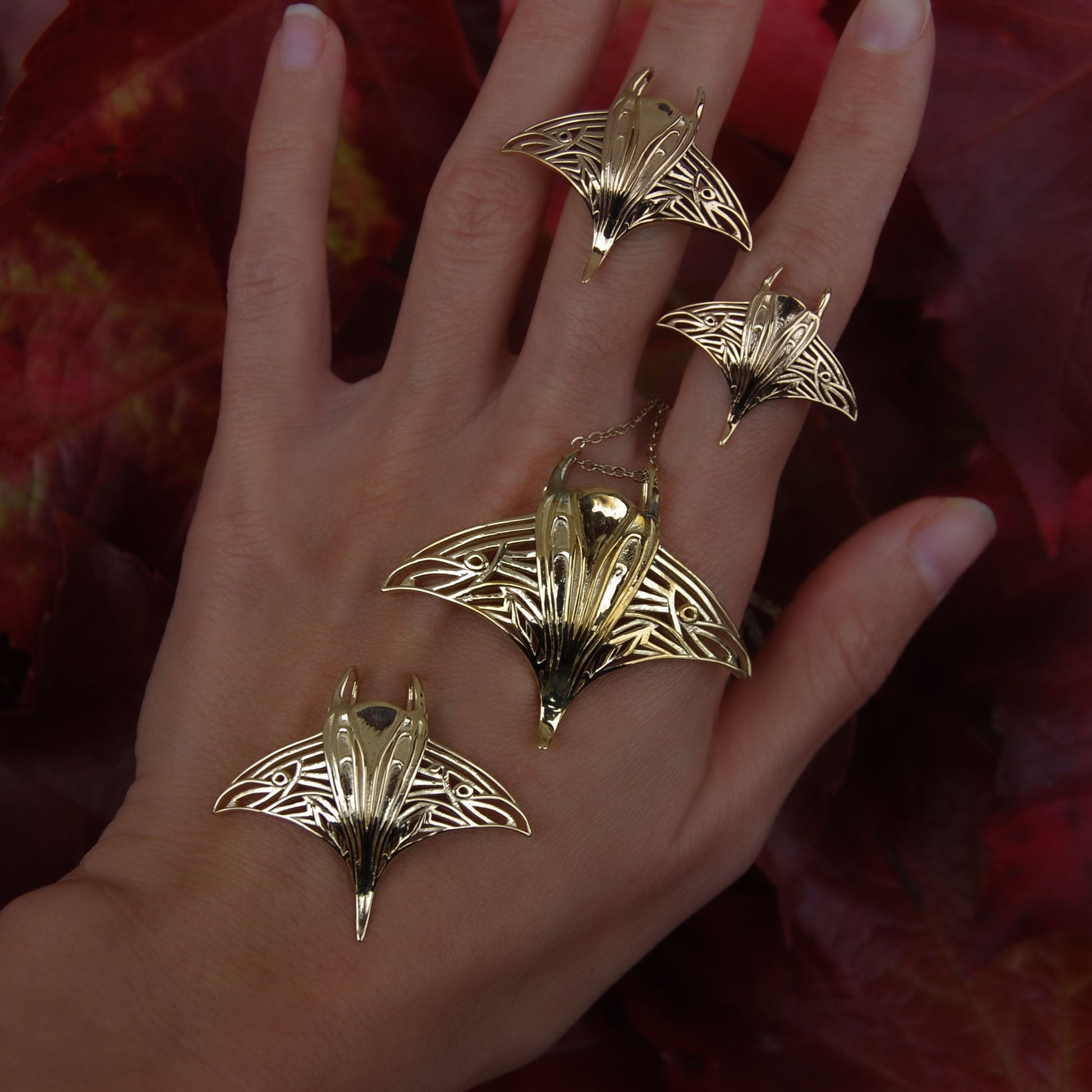 Hand wearing gold manta ray pendant and matching ring, featuring handcrafted ocean jewelry.